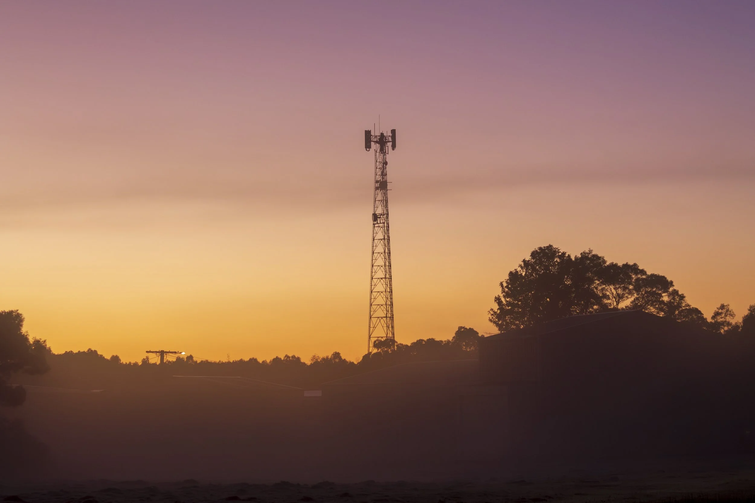 A communications tower rises through the morning fog as dawn breaks over Bairnsdale.