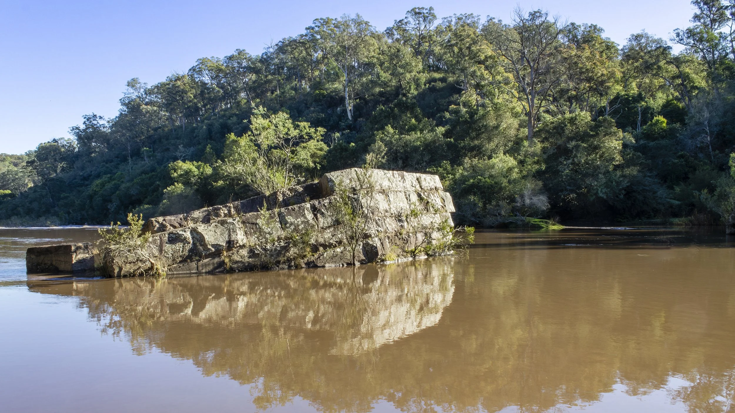 Weir masonry almost submerged in brown floodwater on the Mitchell River