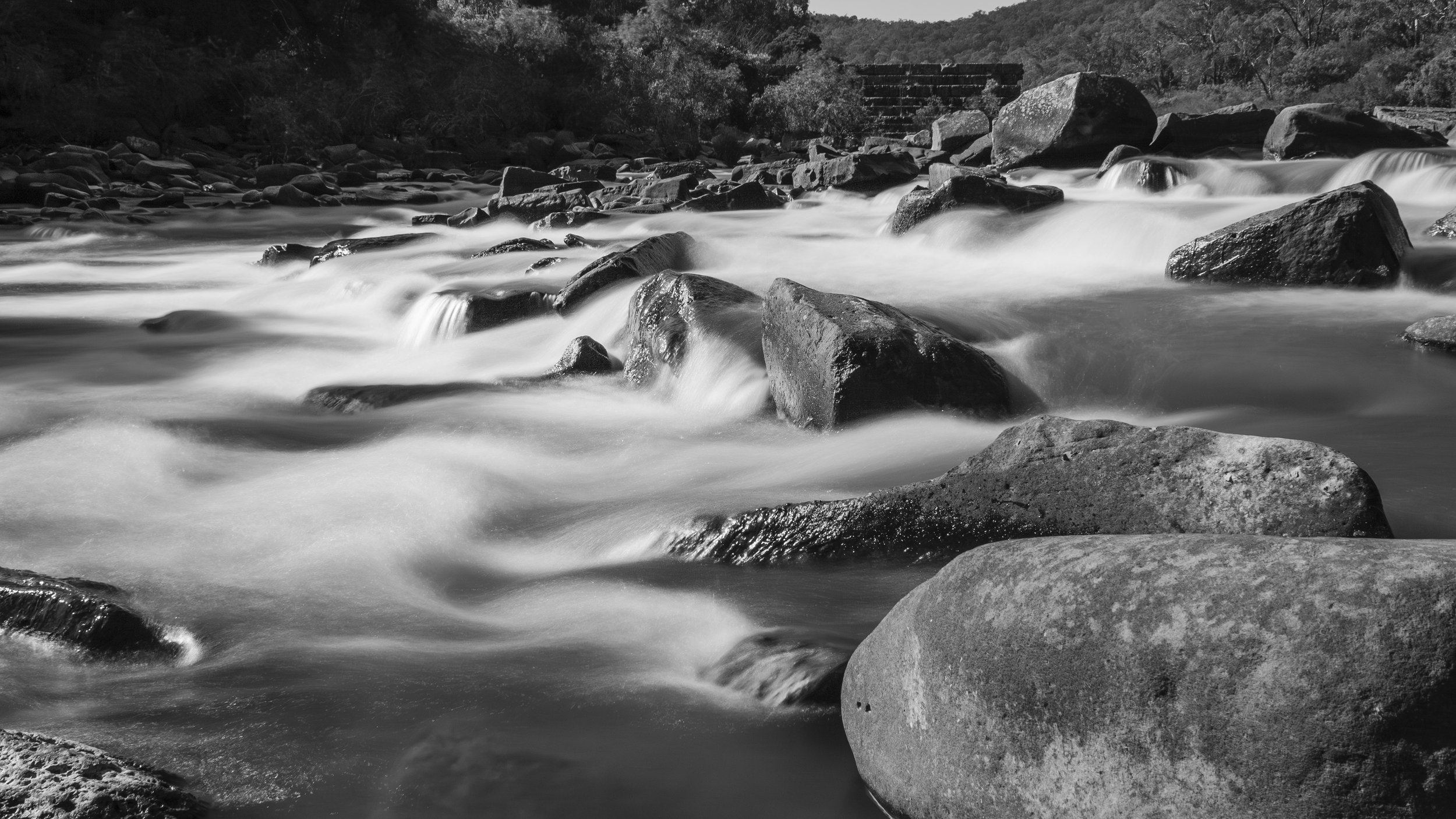 The Glenaladale Weir on the Mitchell River at Wuk Wuk, East Gippsland, Victoria, with the flowing river and surrounding rocks captured in a long-exposure black-and-white photograph.