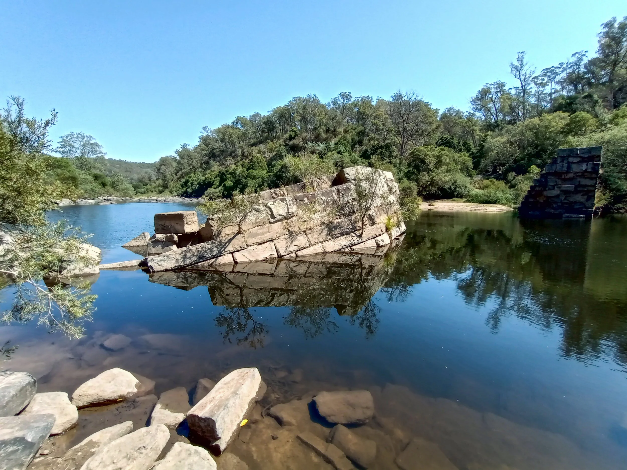 Fallen weir masonry reflected in low, clear water on the Mitchell River