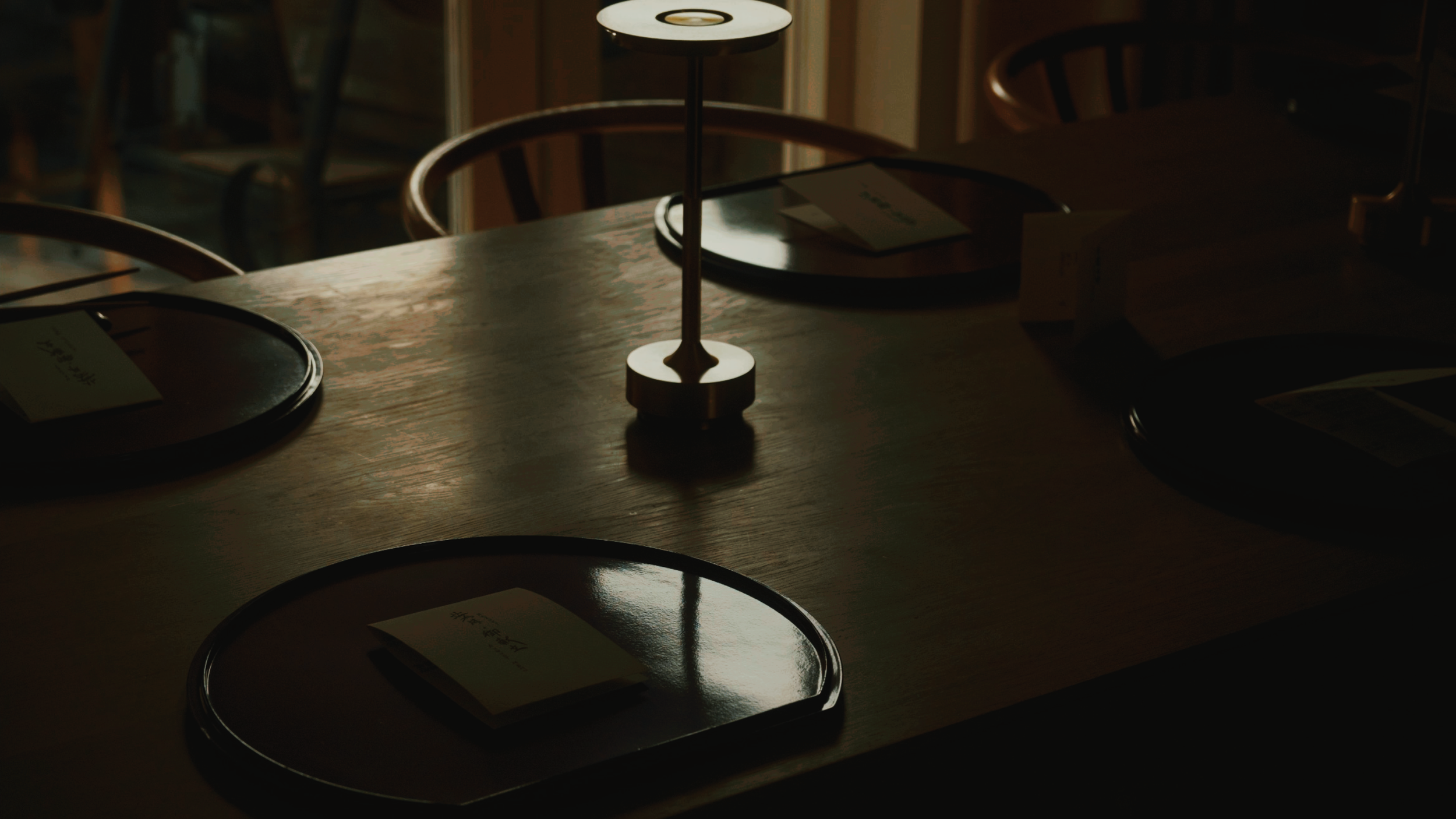 A softly lit dining table set with dark lacquer trays and menus.