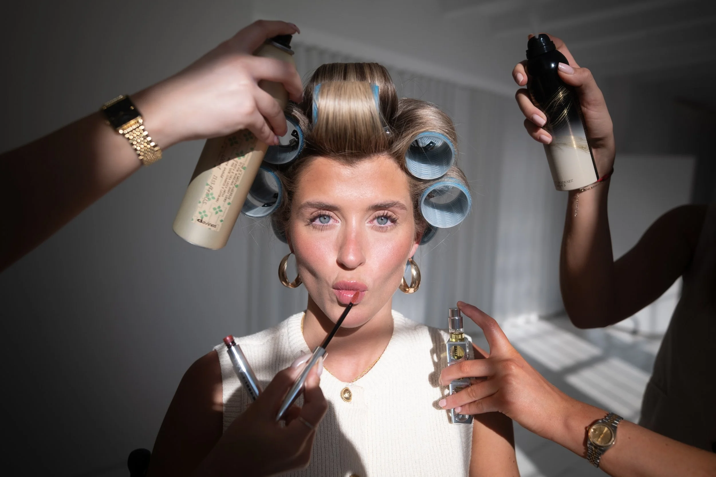 A woman is having her hair put in rollers while she is applying makeup.