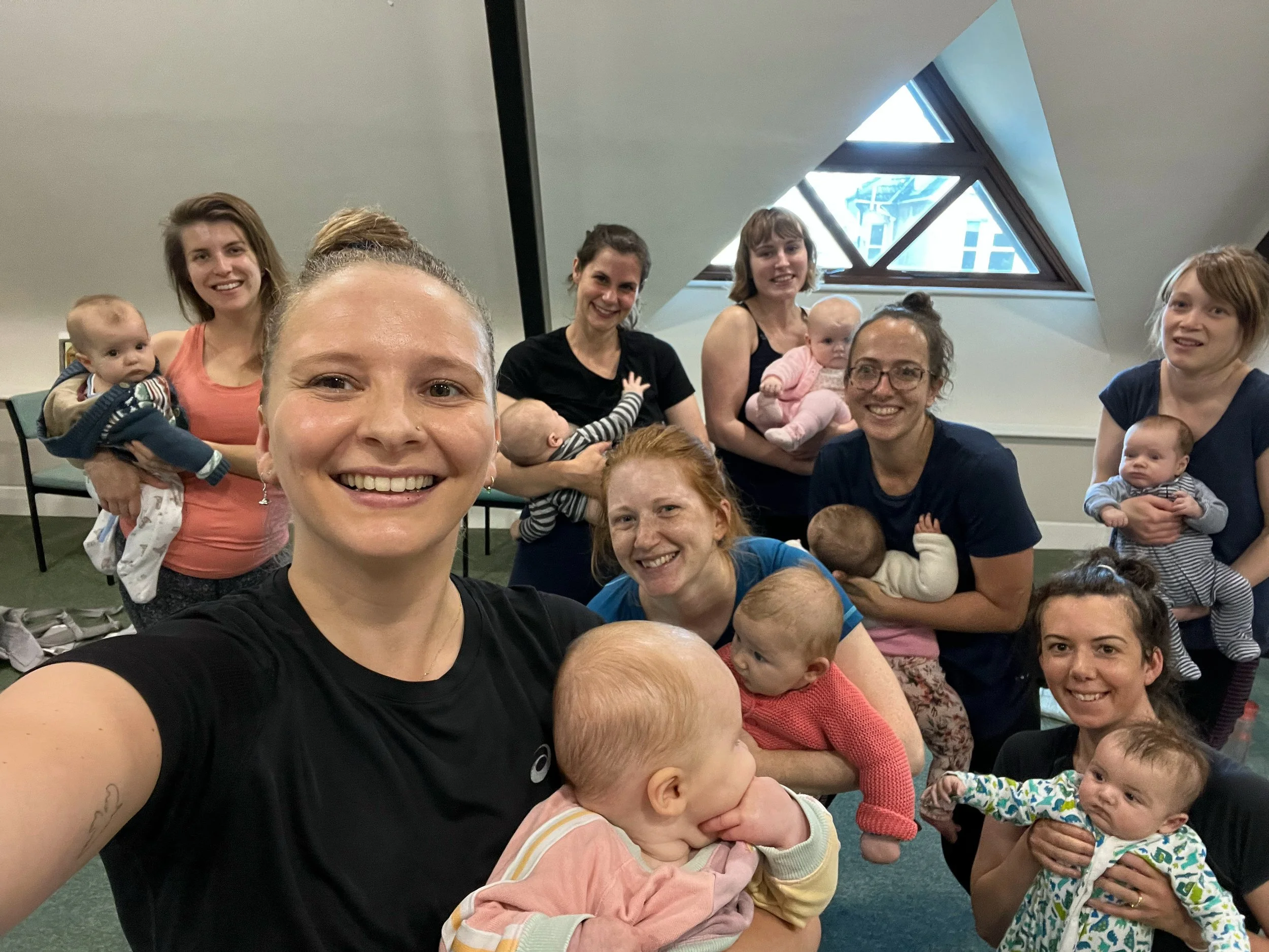 Group of women and babies smiling after a postnatal fitness session.