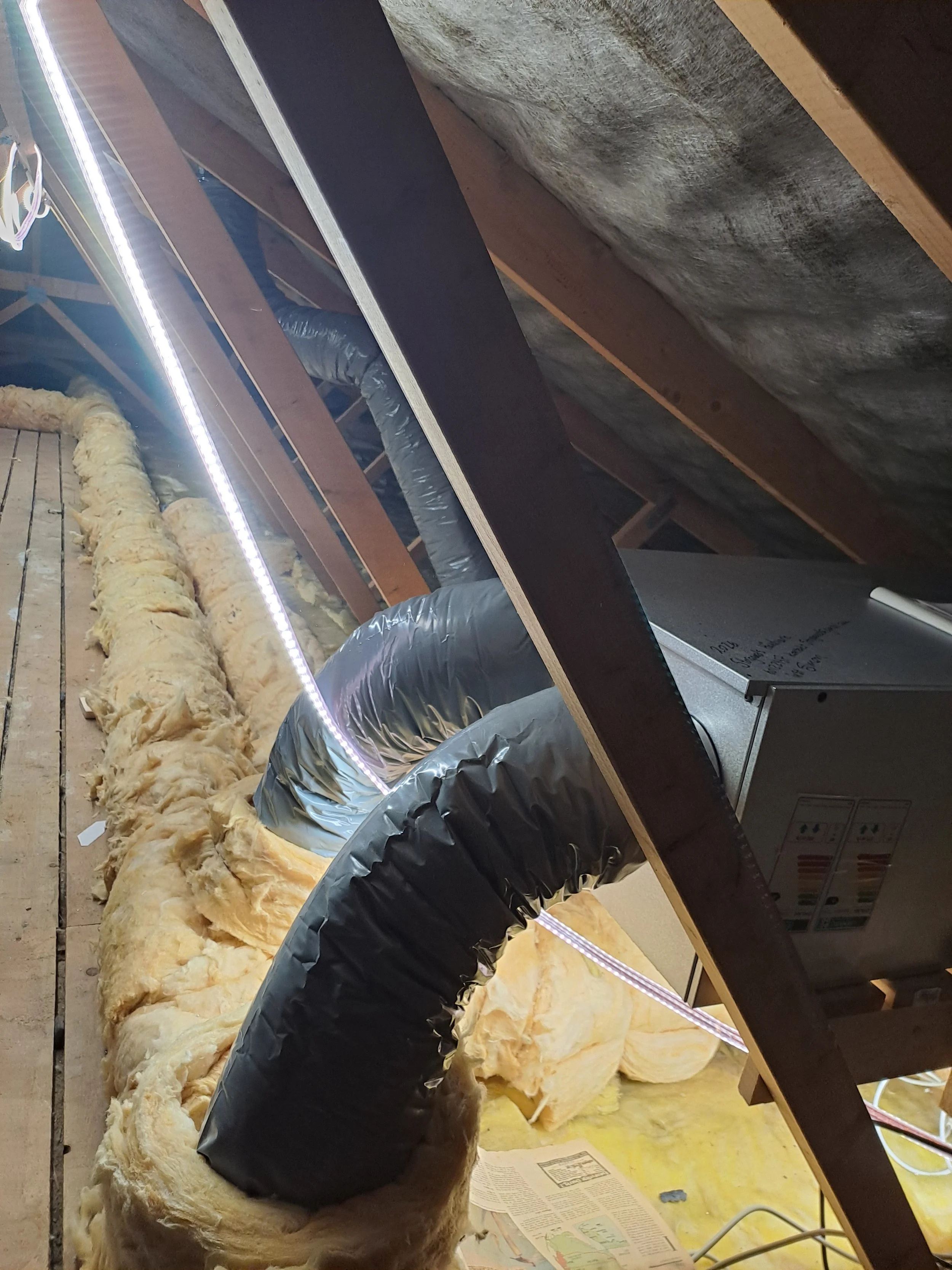 Udsnit af et loftrum under opførelse med synligt isoleringsmateriale og en sort luftkanal, der er dækket til med folie. Der er også en stikkontakt inde i billedet.