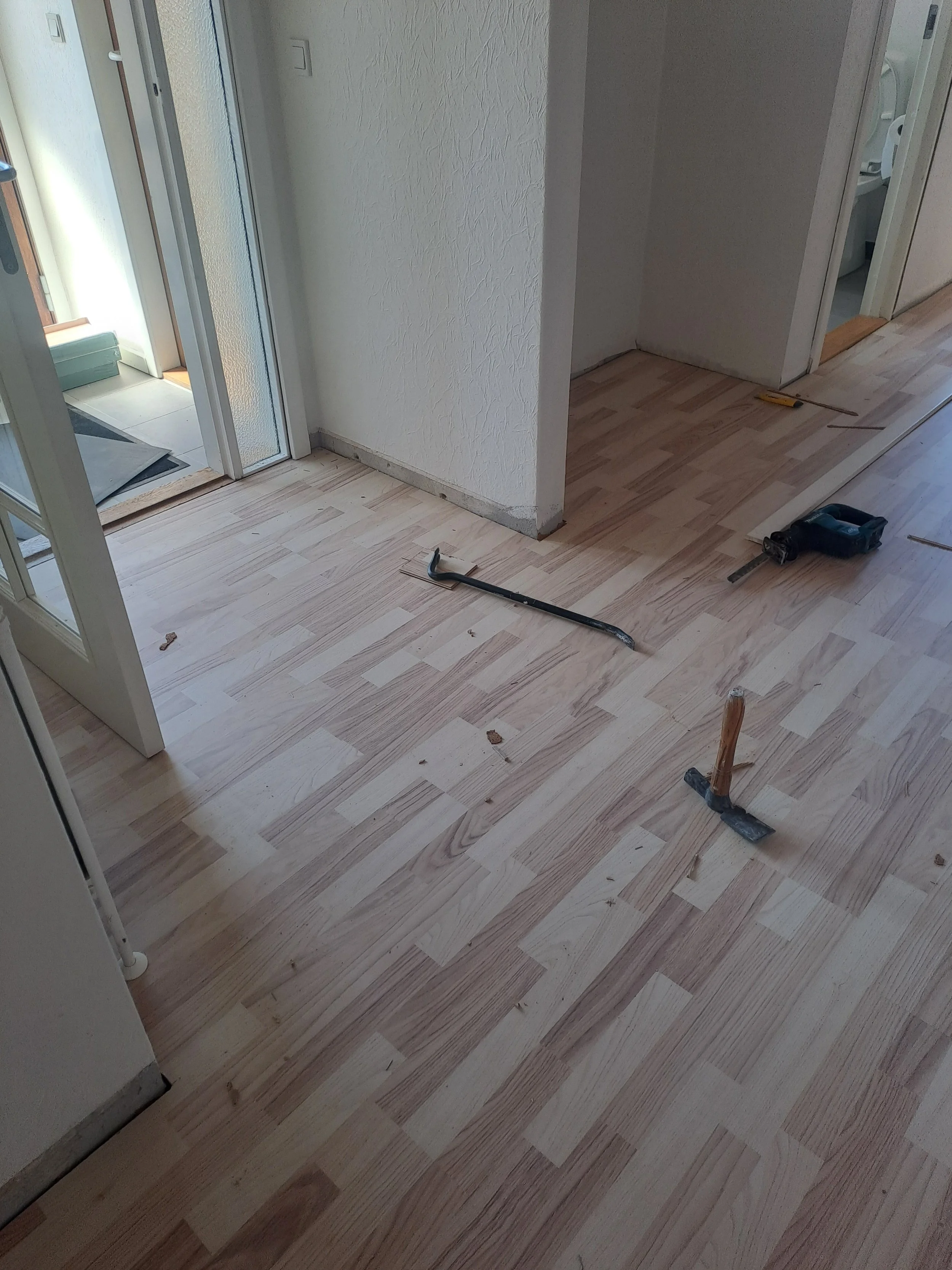 Et rum under renovering med trægulv, værktøj og materialer spredt ud på gulvet, herunder skruetrækker, hammer og målebånd.