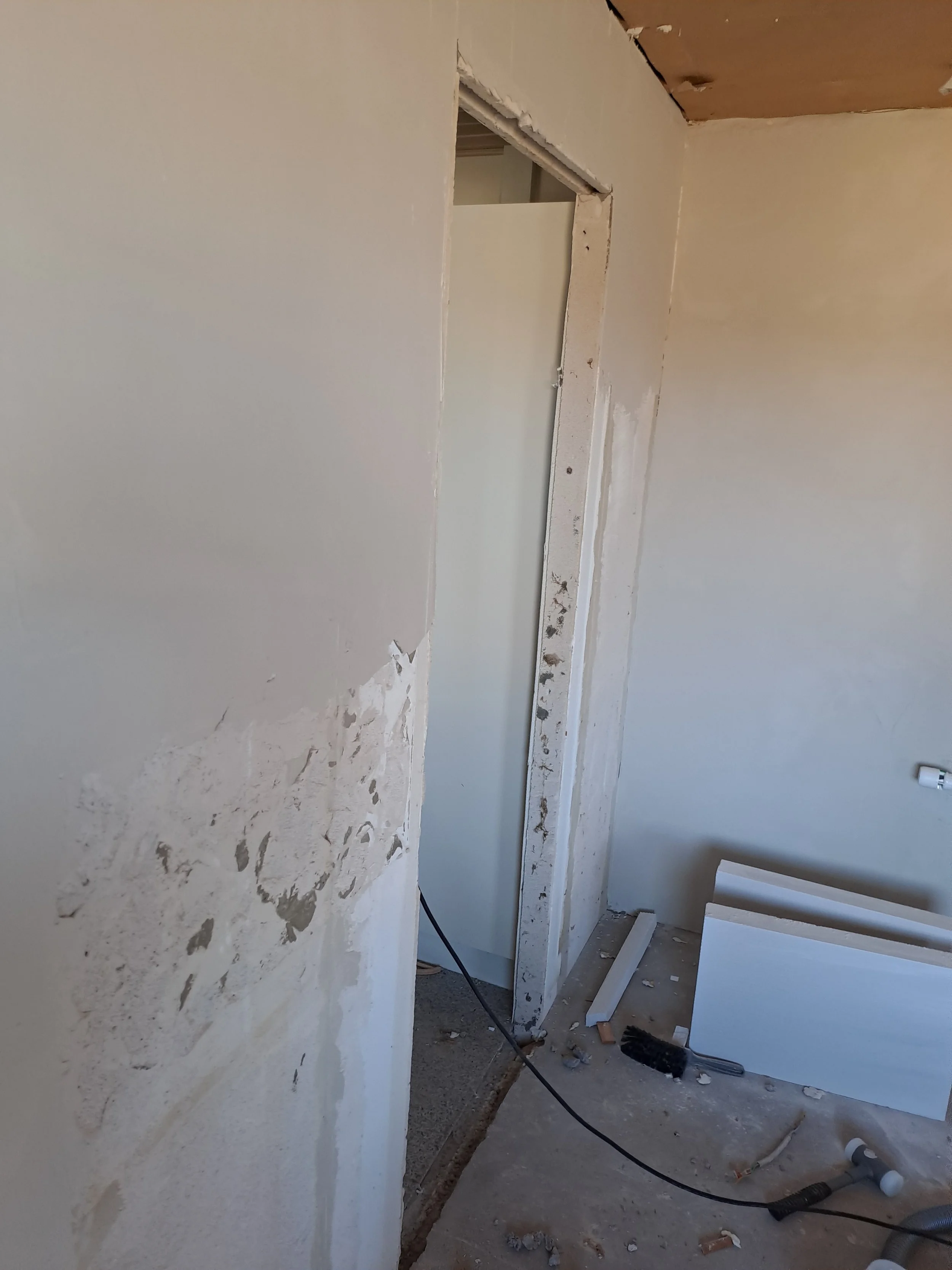 Et værelse under renovering med ubeskyldte vægge, værktøj og byggematerialer på gulvet.