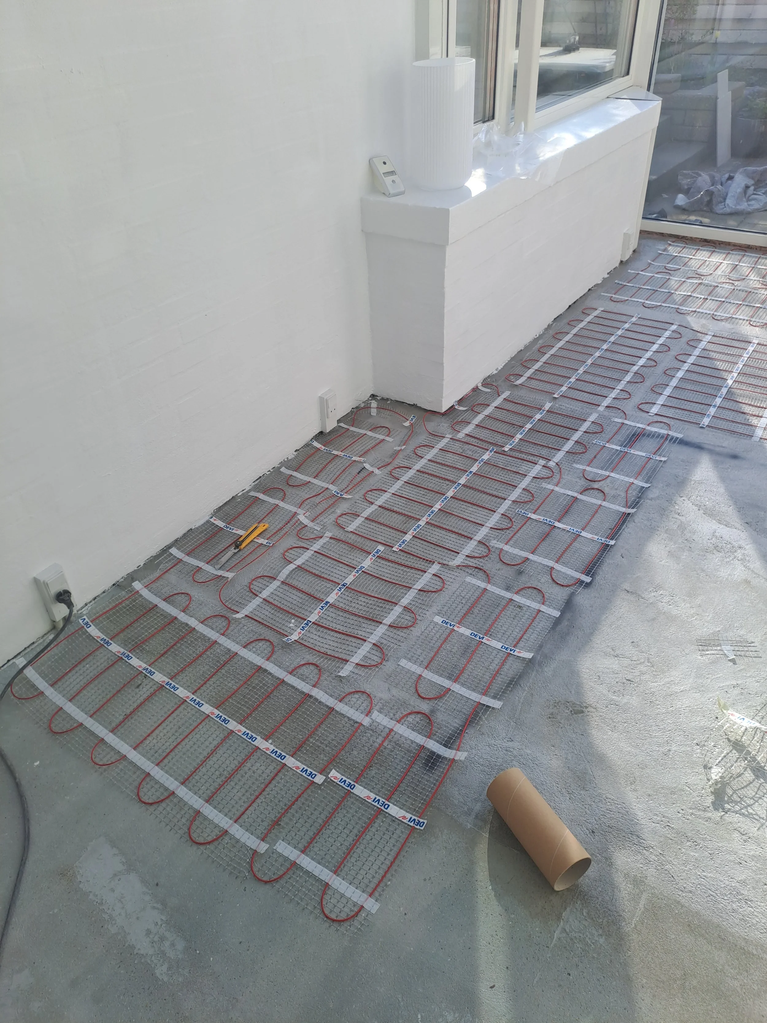 Installation af gulvvarme med varmeslanger og undergulv forfra i et rum under konstruktion.