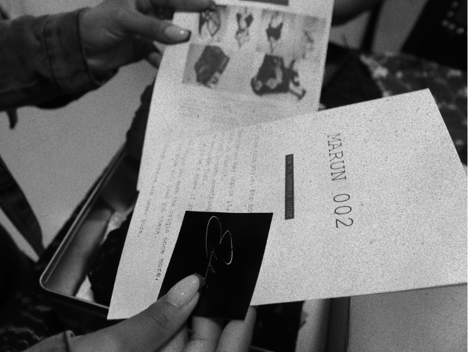 Person holding a small photo of a signature with a hand in the background holding an item with dog illustrations.