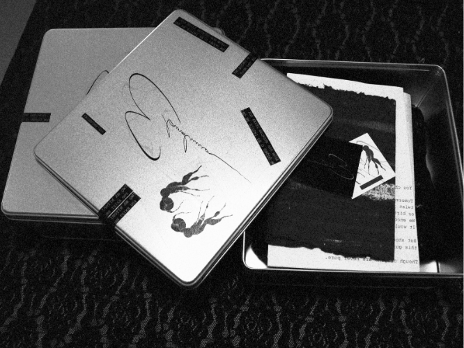 Stack of autograph books or magazines with signatures on the covers, placed on a patterned fabric surface, with some papers or photos inside a small metal or plastic tray nearby.
