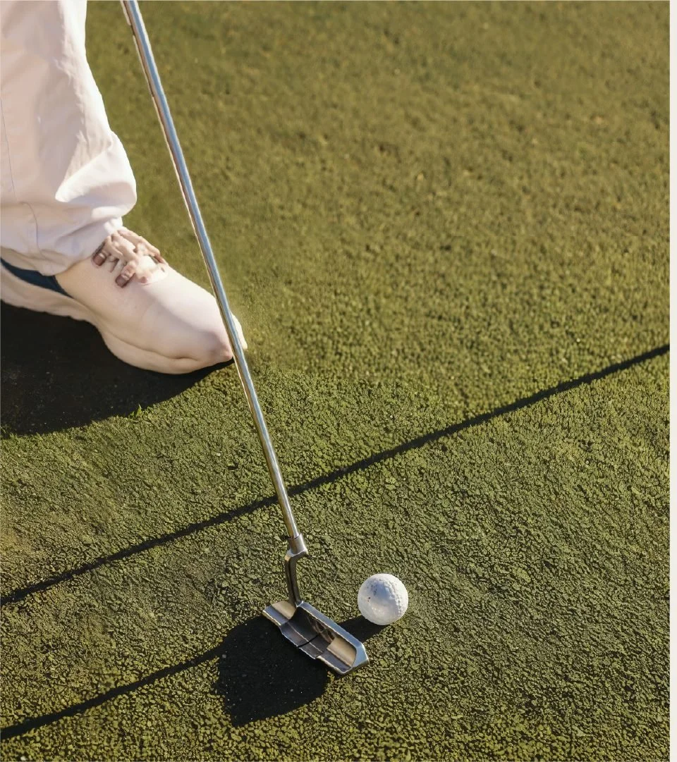 Close-up of a person in white clothing preparing to hit a golf ball on a green putting surface with a putter