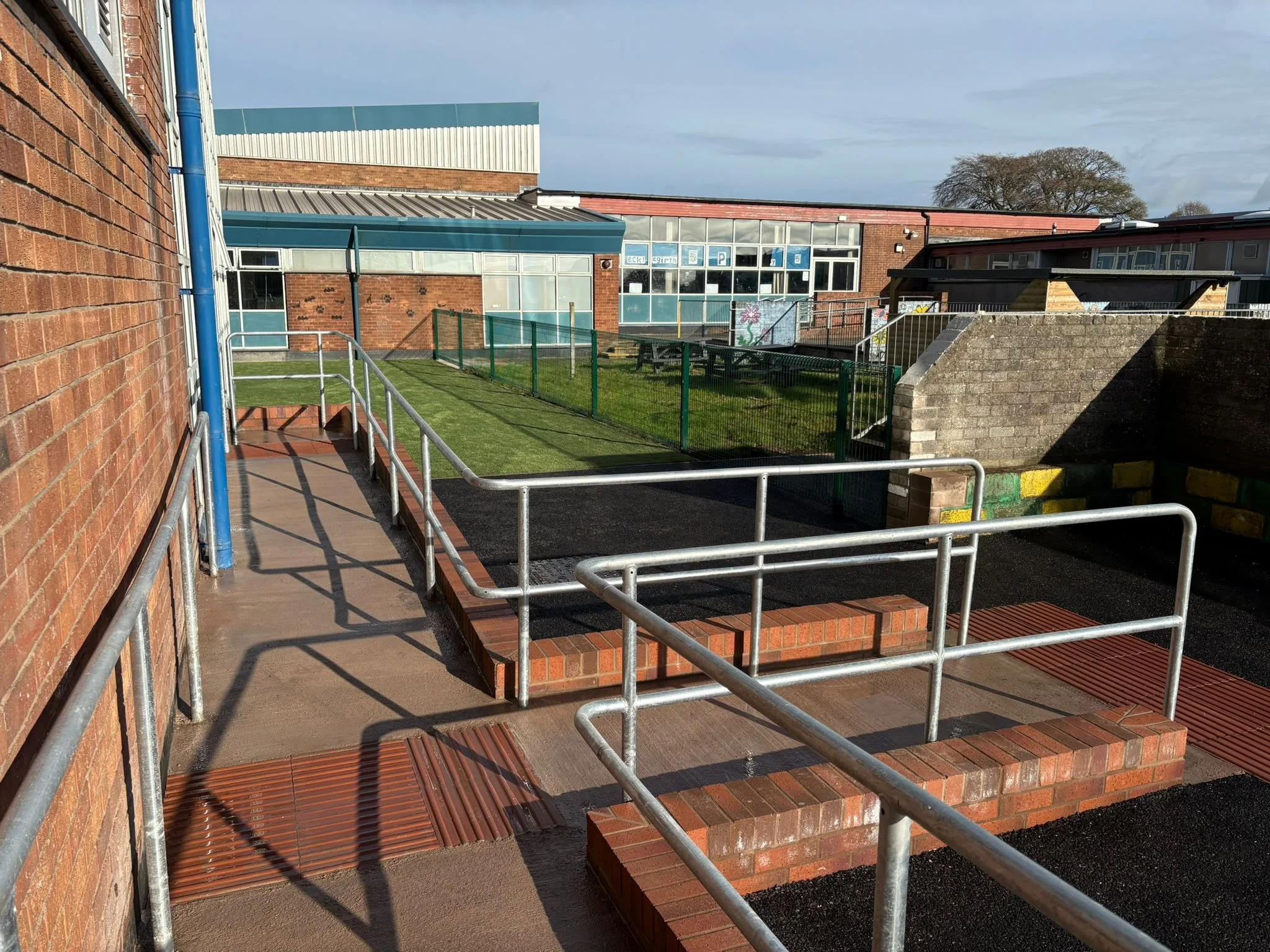 New external accessible ramp, brick steps and galvanised handrails between school buildings.