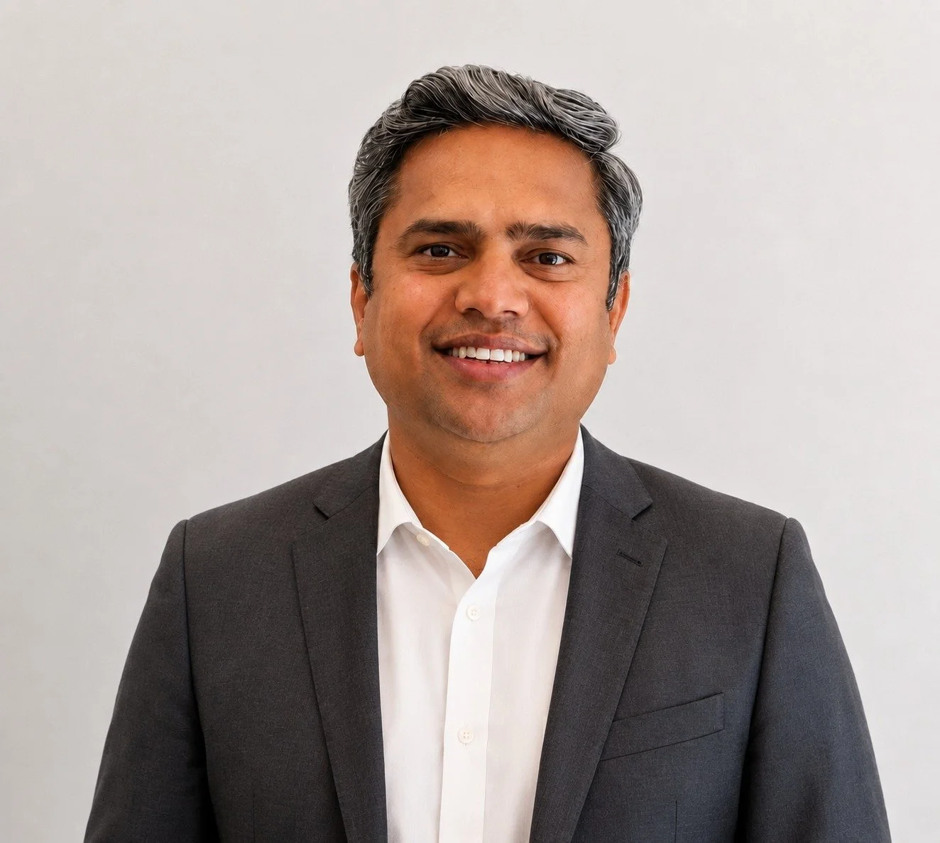 Professional man in a gray suit and white shirt smiling against a plain background.
