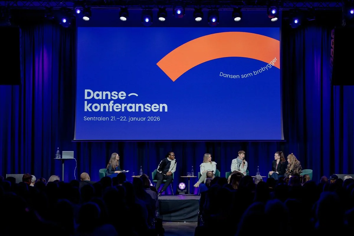 Paneldiskusjon under Danse-konferansen 2026, med fem personer på scen, stor skjerm med logo og tekst, mørk teaterbelysning, fullt publikum