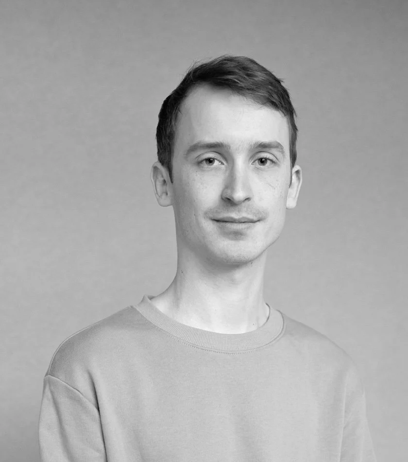 Svart-hvitt portrett av en ung mann med kort hår, iført en enkel genser, smilende litt, med en nøytral bakgrunn.