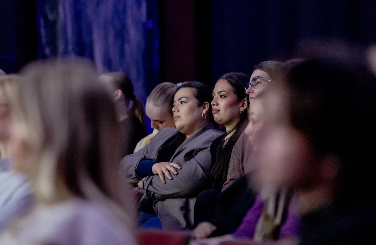 En gruppe mennesker som deltar på en konferanse eller et seminar, sitter i rader og lytter opmerksomt.