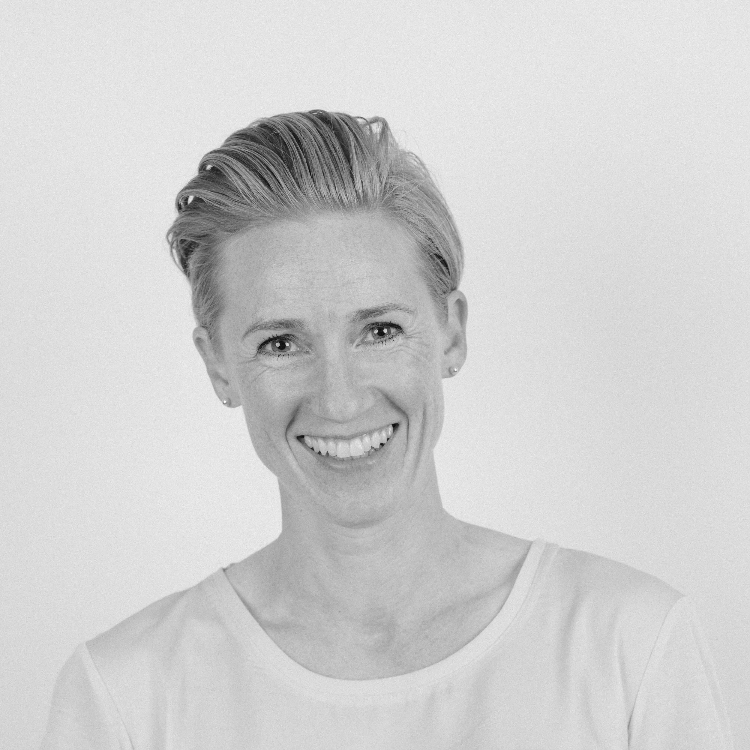 Et svart-hvitt bilde av et kvinnesmil, med kort, lyst hår og bølgete hår, iført en hvit topp.