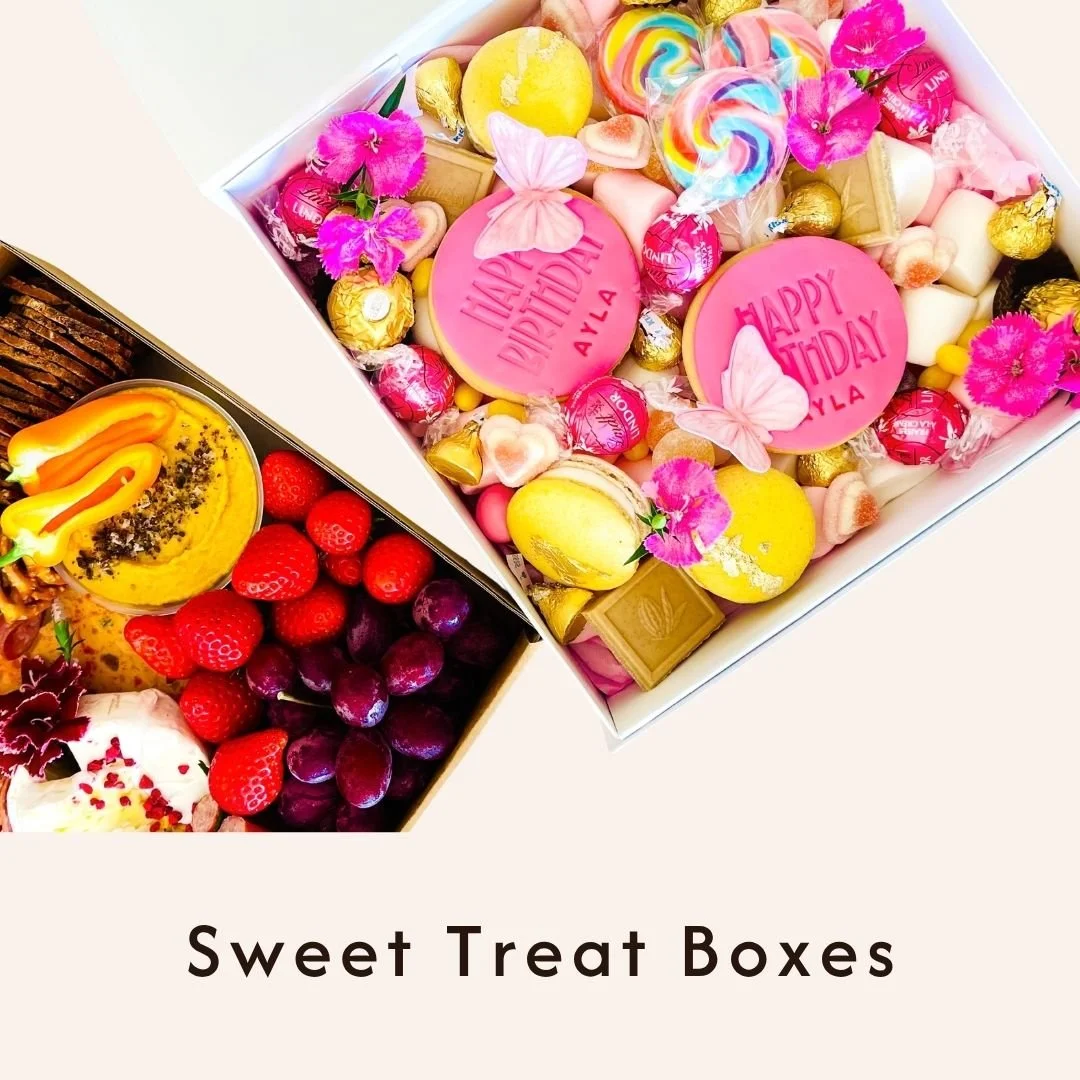 Two gift boxes filled with colorful candies and desserts, decorated with pink donuts, butterflies, and flowers, labeled for birthday and holiday celebrations, with fresh strawberries, grapes, and a decorated cake below.