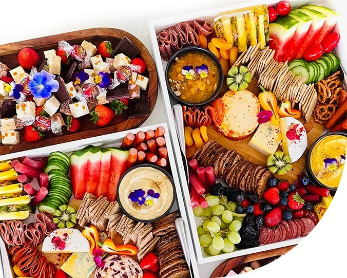 Colorful charcuterie boards with sliced fruits, cheeses, meats, crackers, and dips, topped with edible flowers.