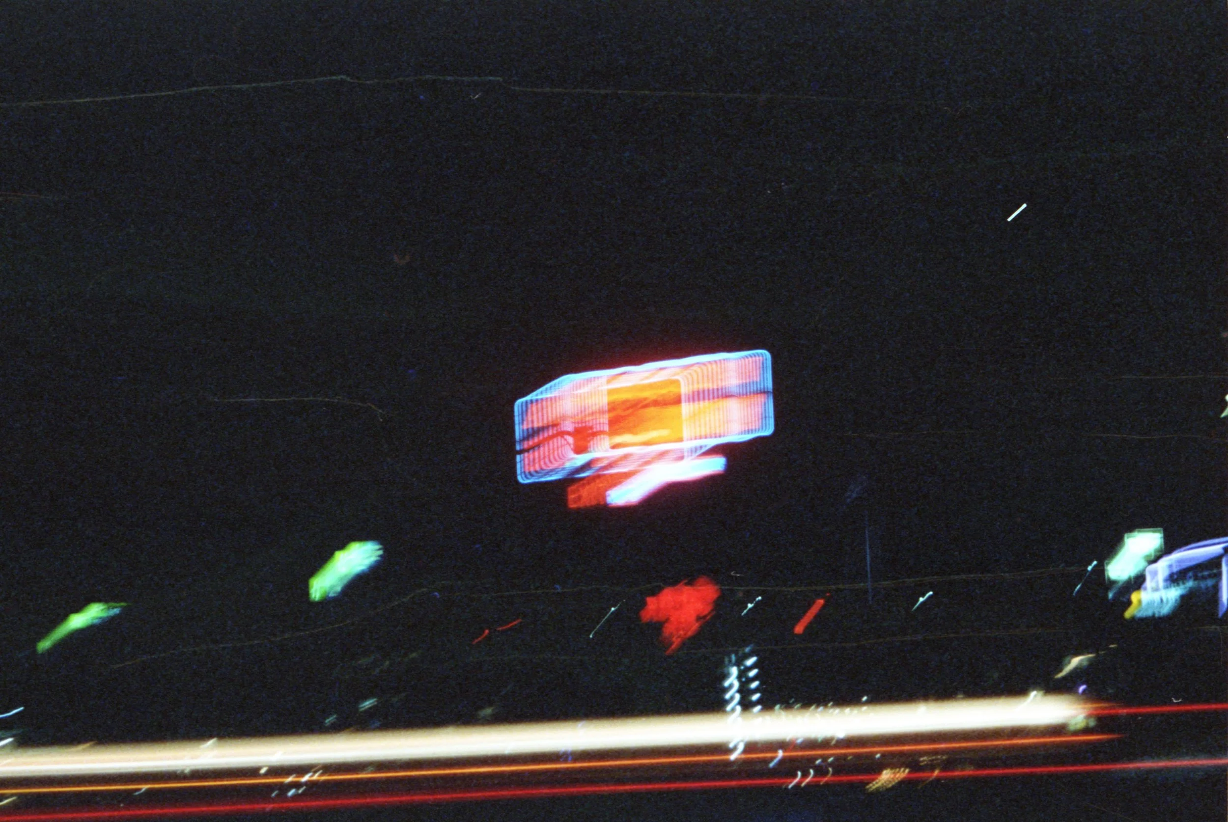 Nighttime scene of moving neon lights from vehicles and signs, creating blurred light trails.