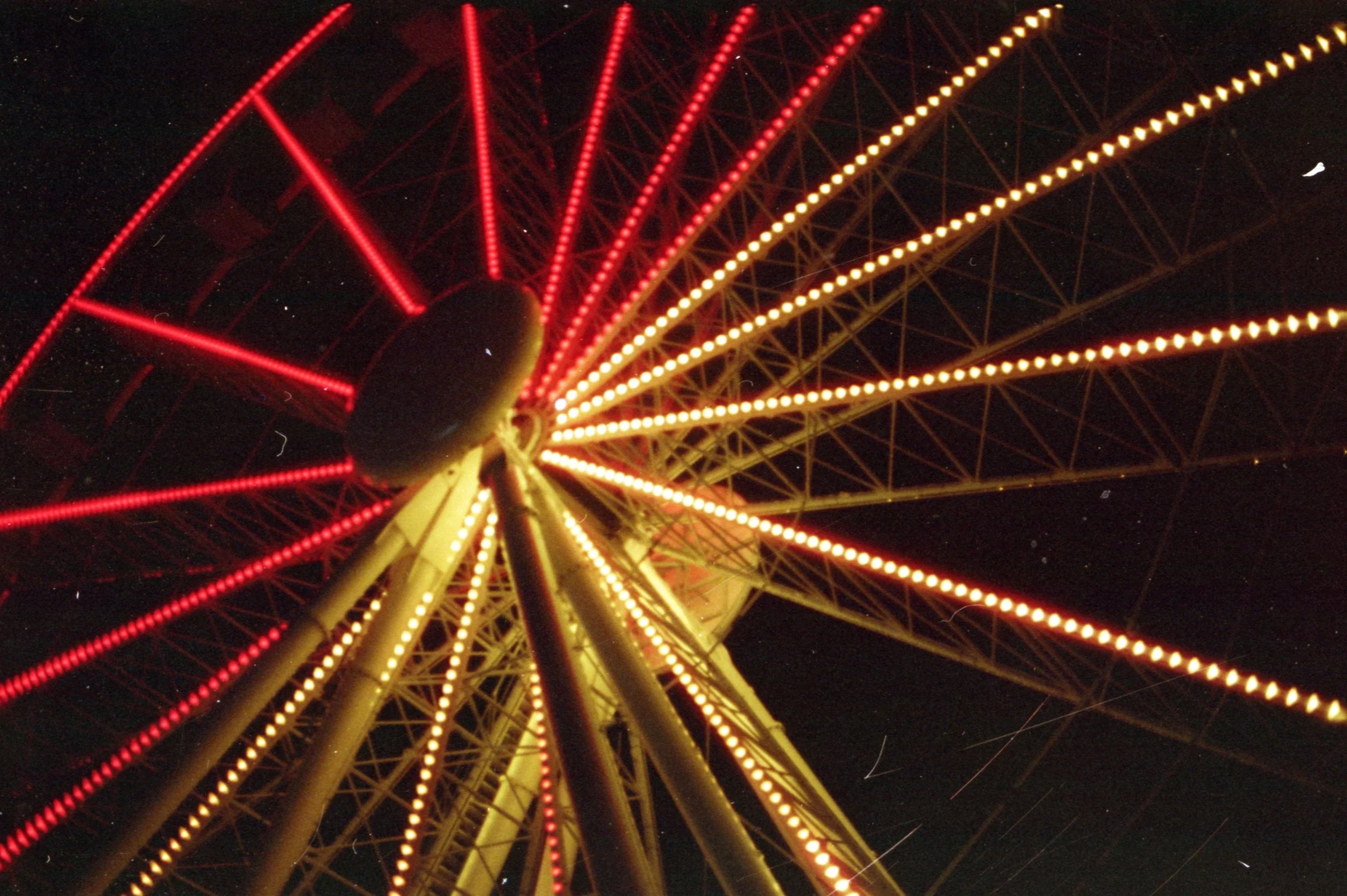 Nighttime view of a Ferris wheel with red and yellow lights illuminating its structure.