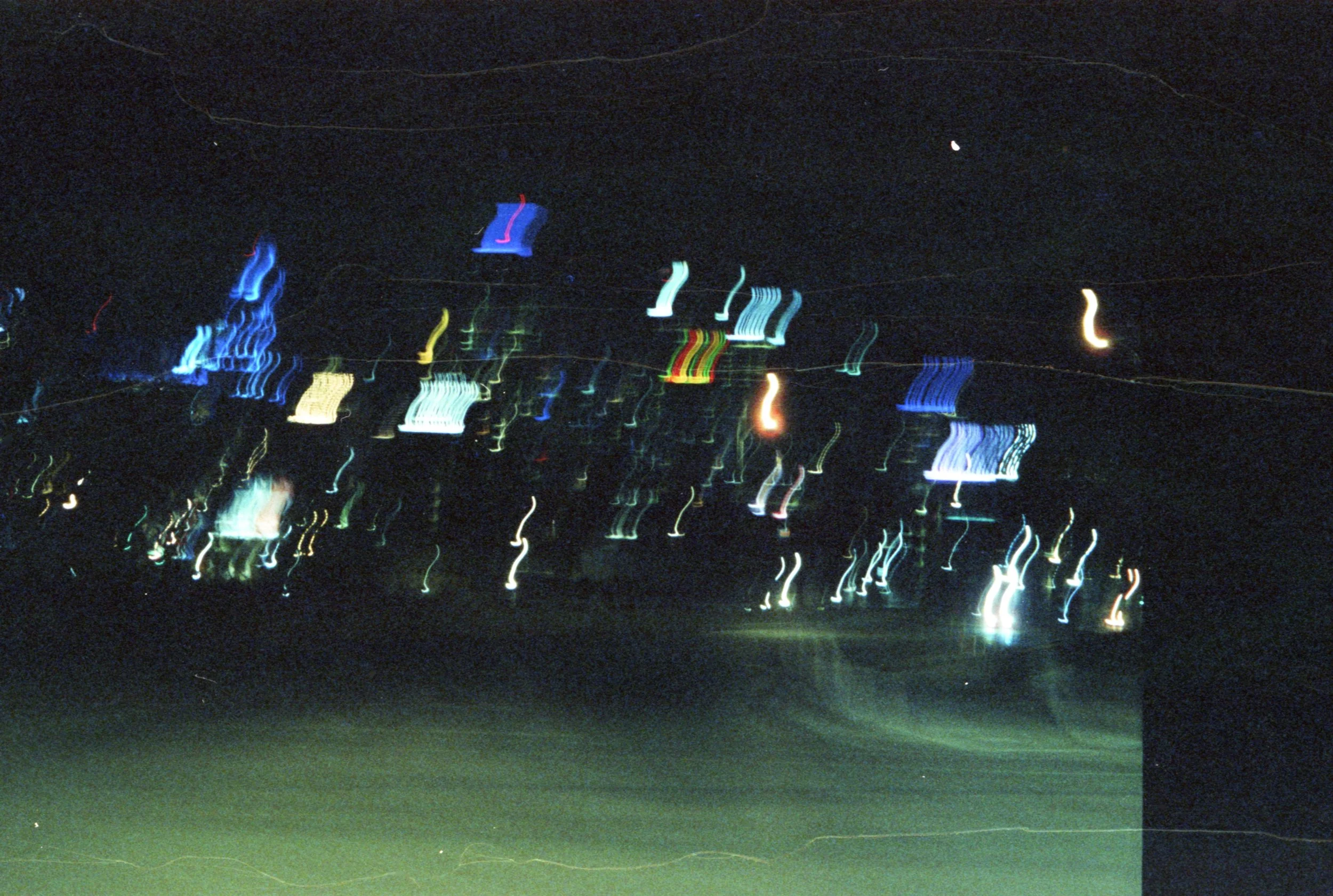Nighttime cityscape with blurred multicolored lights creating streaks against a dark sky.