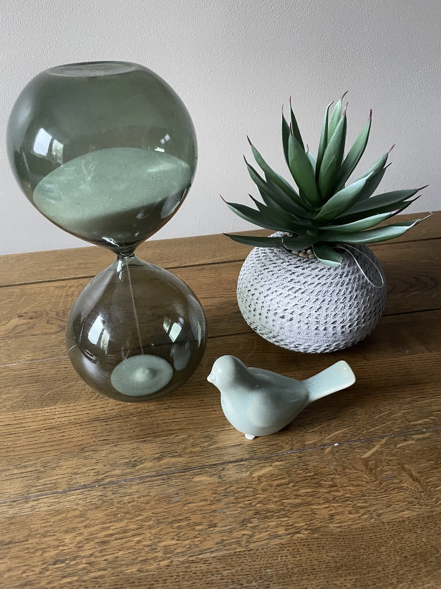 Green sand timer with grains running through, green bird ornament and small plant in a pot