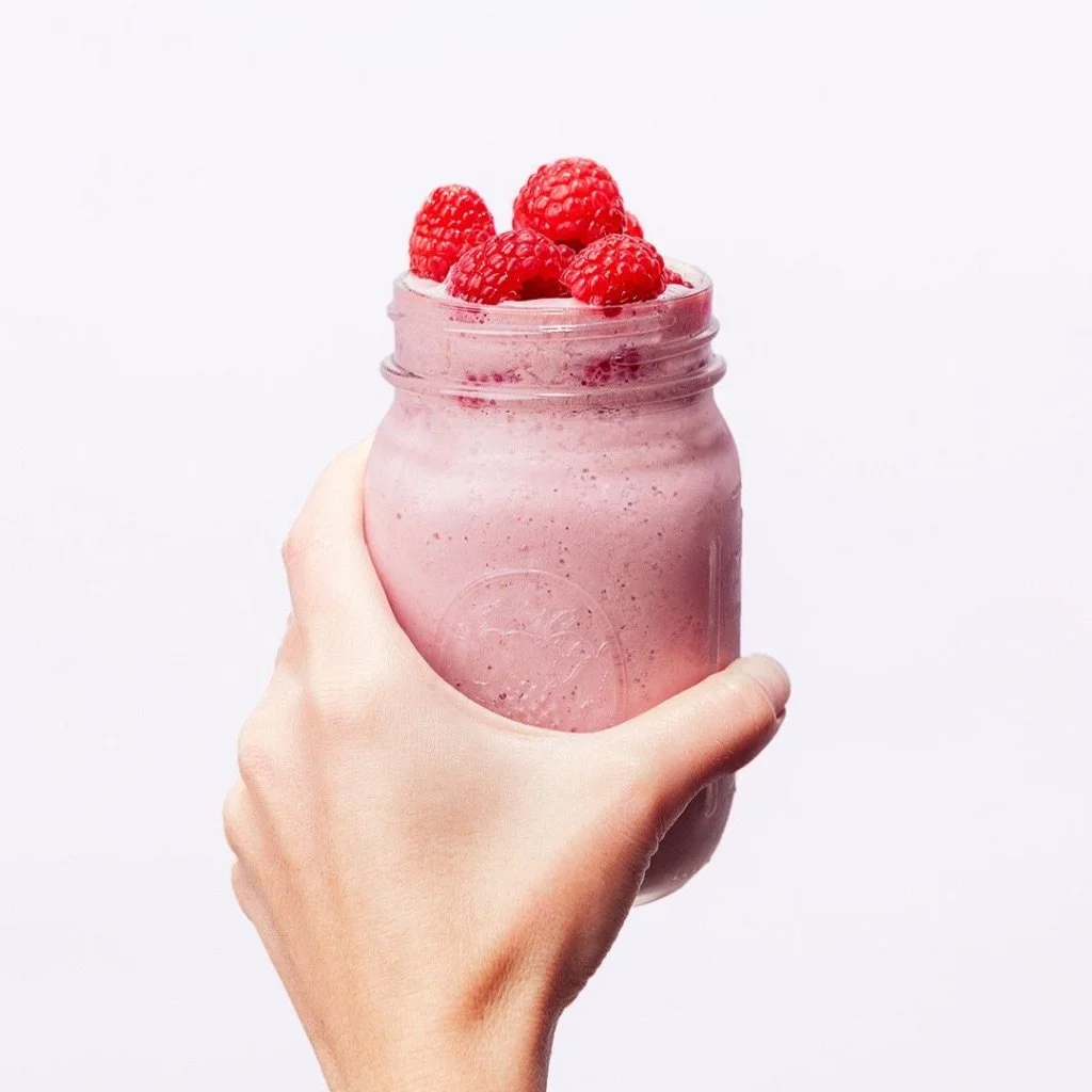 A hand holding a glass jar filled with pink smoothie topped with fresh raspberries.