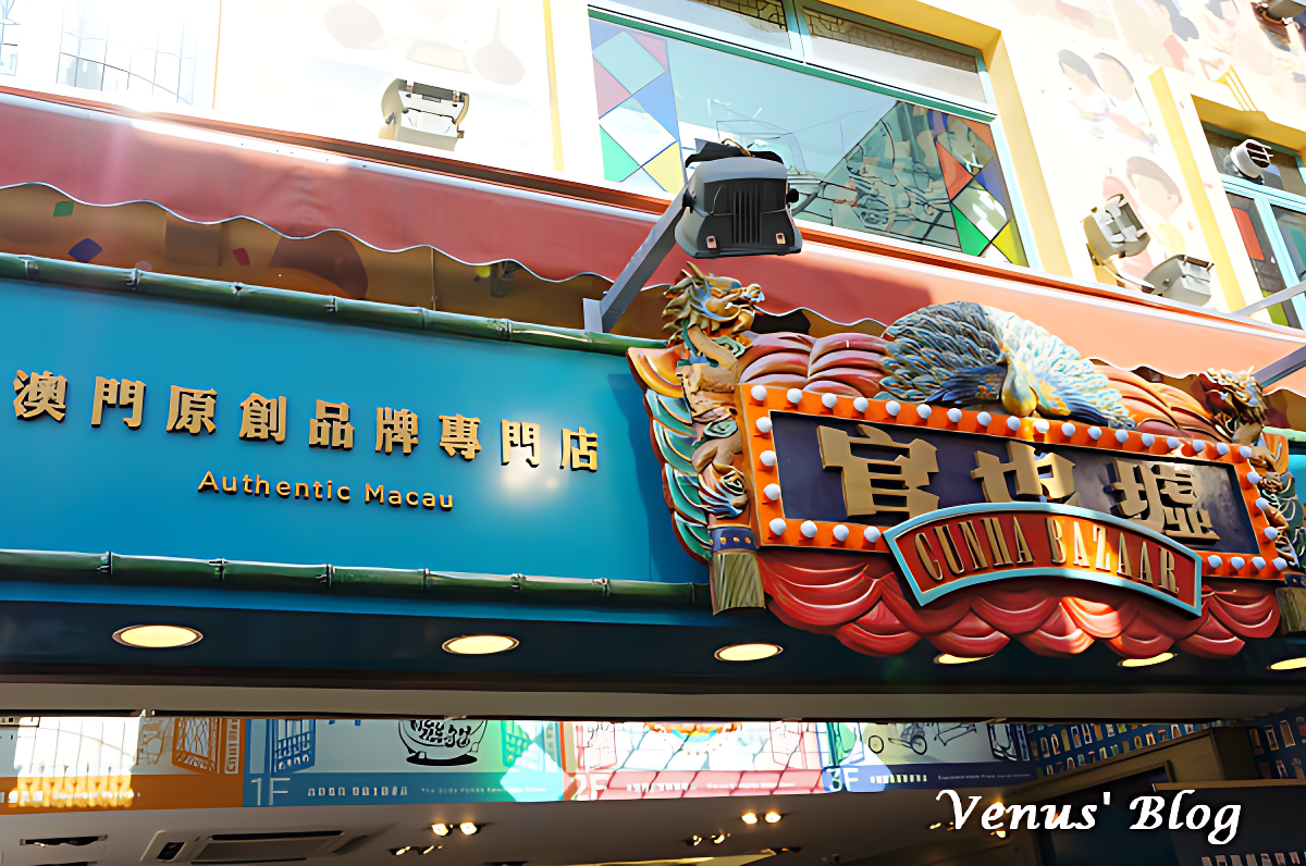 Signage for a Guniya Bazaar on a building with decorative dragons and peacocks and Chinese characters. The sign also has English text saying 'Authentic Macau' and 'Guniya Bazaar'.