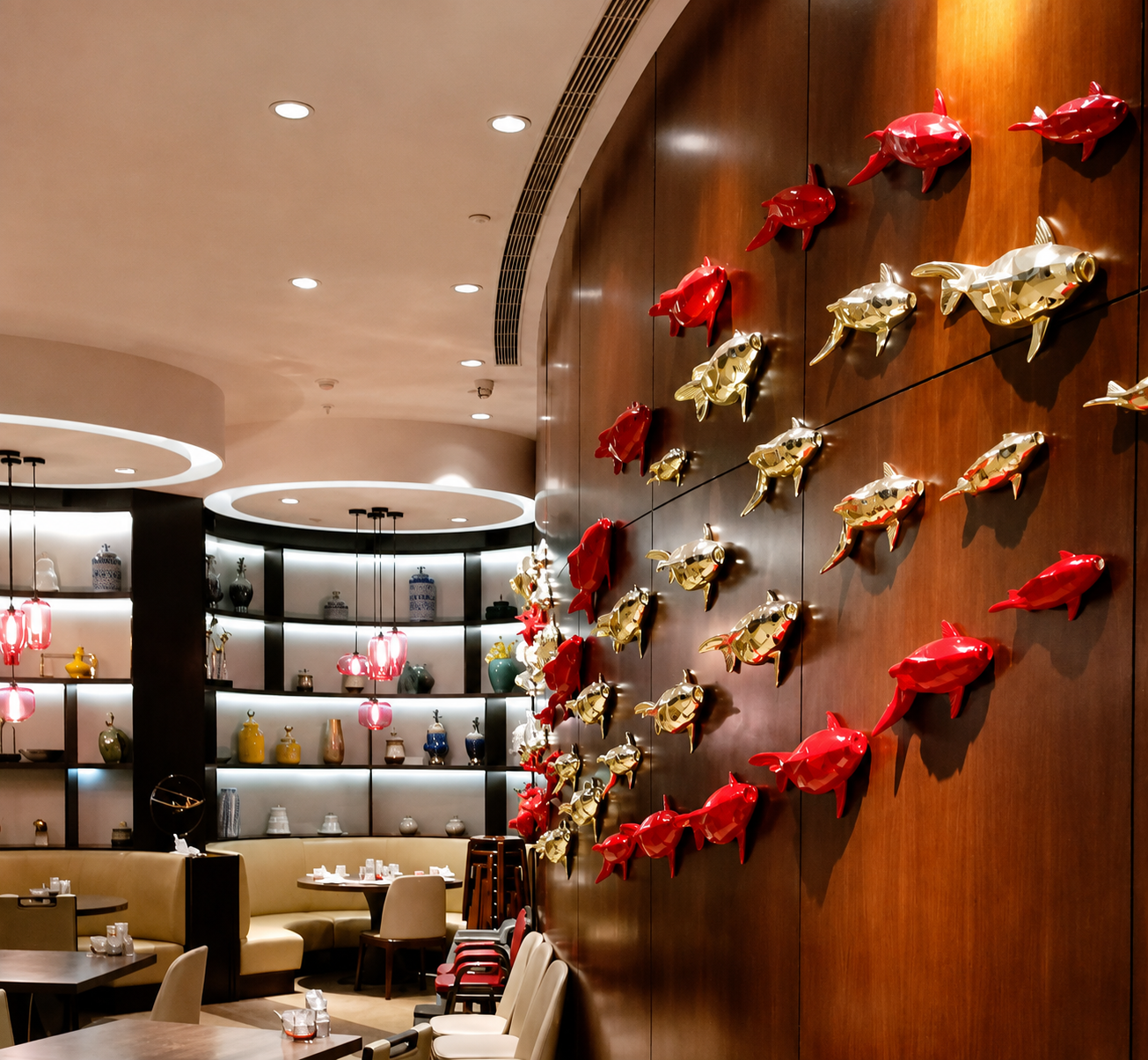 Decorative wall with red and gold fish sculptures in a restaurant interior with shelves of ceramics and pink pendant lights.