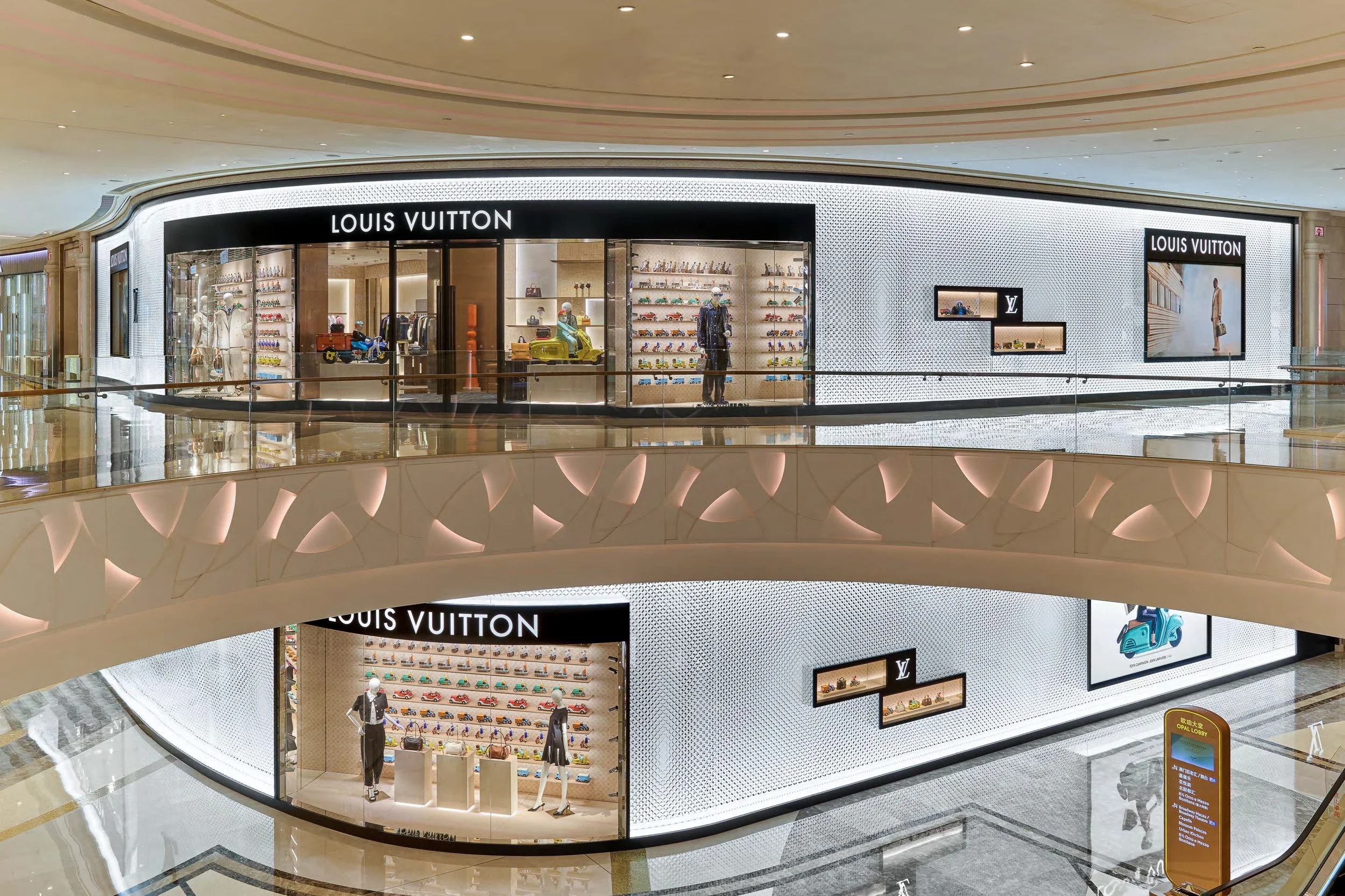 Interior of a Louis Vuitton store in a shopping mall with mannequins and display shelves showcasing handbags, shoes, and accessories.