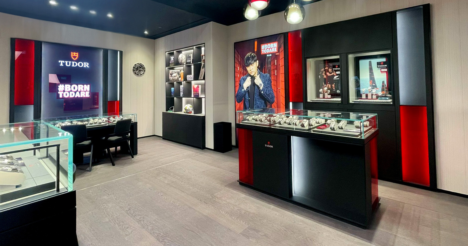 Interior of a luxury watch store showcasing Tudor watches, with display cases, a poster of a model, and watch displays featuring the brand's logo and branding.