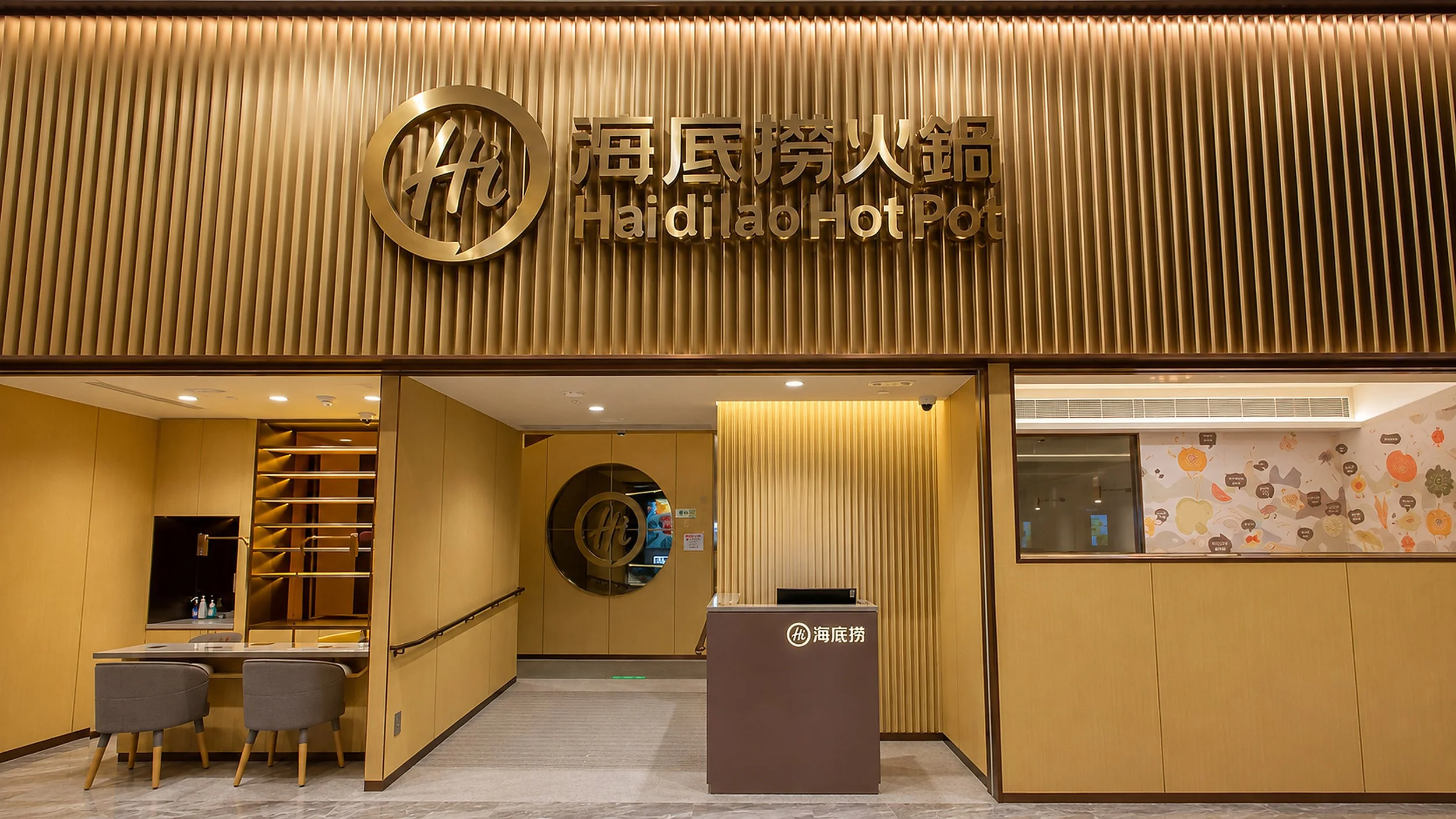 The entrance to Haidilao Hot Pot restaurant with a gold-colored sign displaying its name in both Chinese characters and English, featuring a modern and stylish interior design with wood accents and a decorative wall.