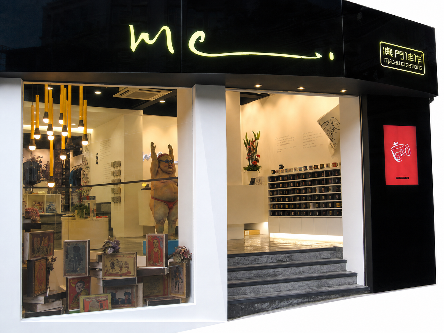 View of a modern storefront with large glass windows, displaying a sumo wrestler statue and artwork inside, with a black signboard and neon signs in English and Chinese.