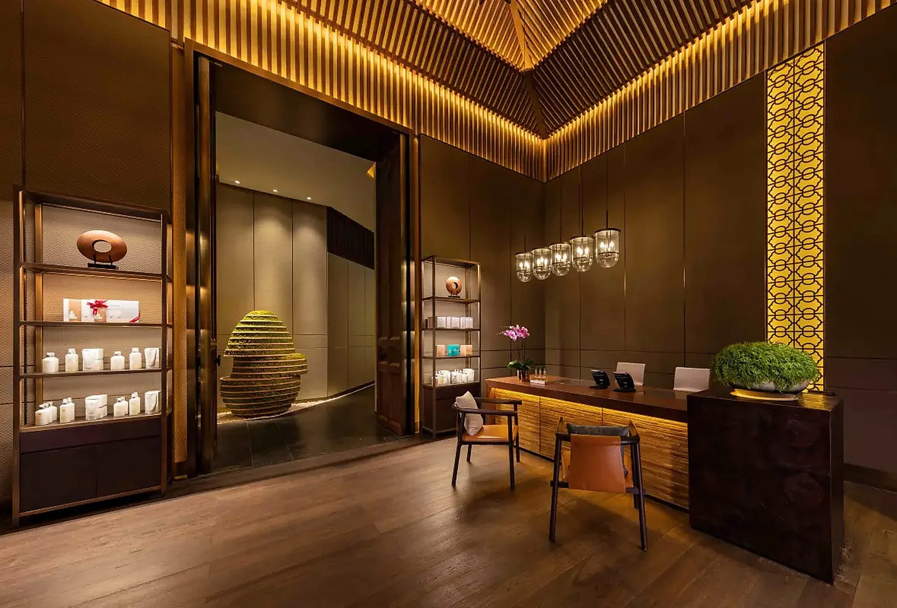 Lobby reception area with wooden accents, modern lighting, potted plants, and display shelves.
