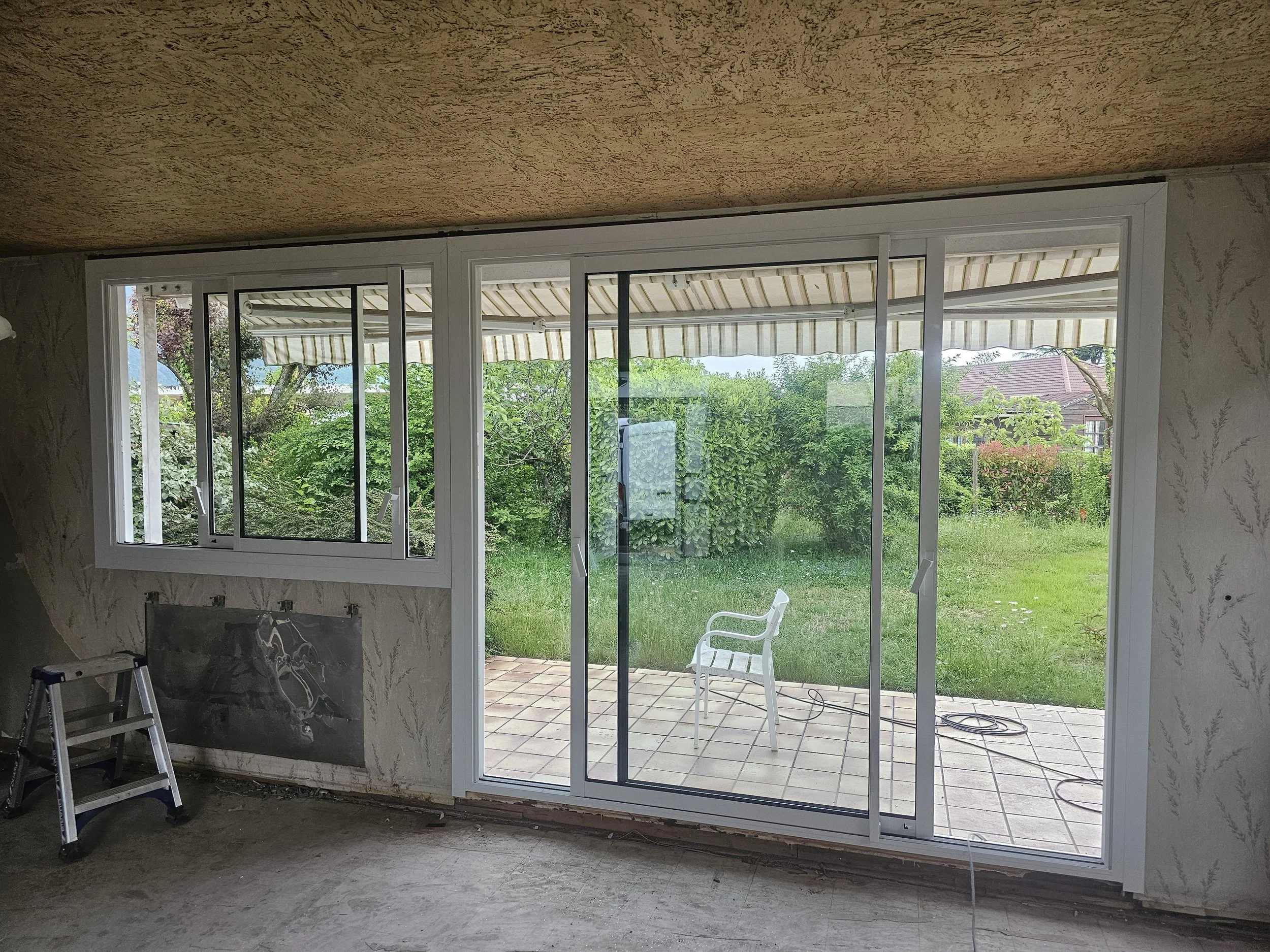 Une grande fenêtre avec une fenêtre coulissante qui donne sur un jardin verdoyant avec un toit en terrasse en dehors.