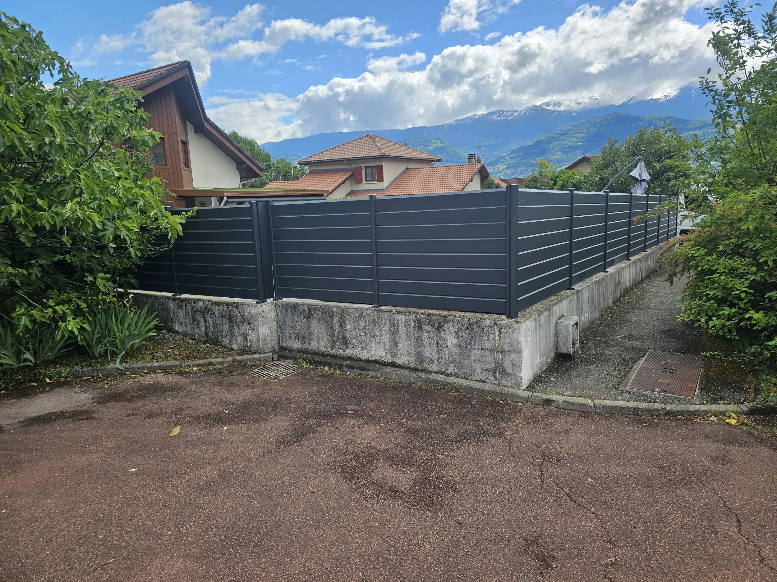 Vue d'une maison avec toit en tuiles rouges, entourée de végétation et avec des montagnes enneigées en arrière-plan.