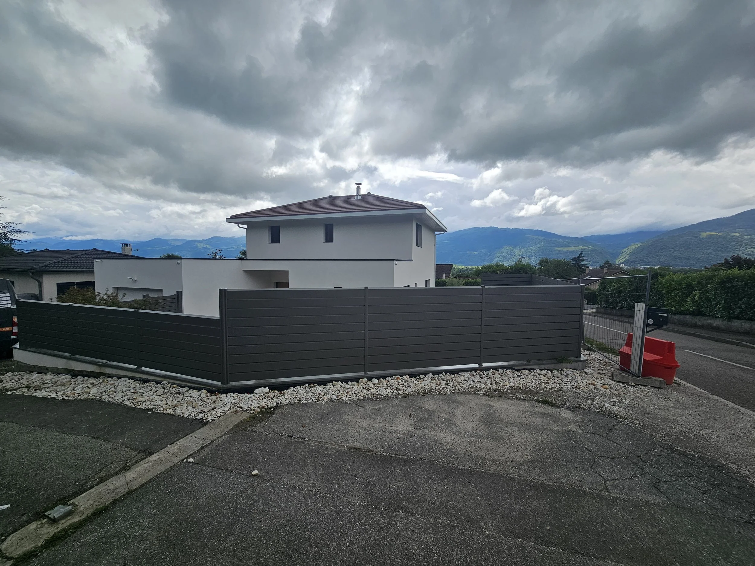 Vue sur un bâtiment moderne blanc avec un toit en pente, avec des montagnes en arrière-plan. Ciel orageux avec de gros nuages gris.