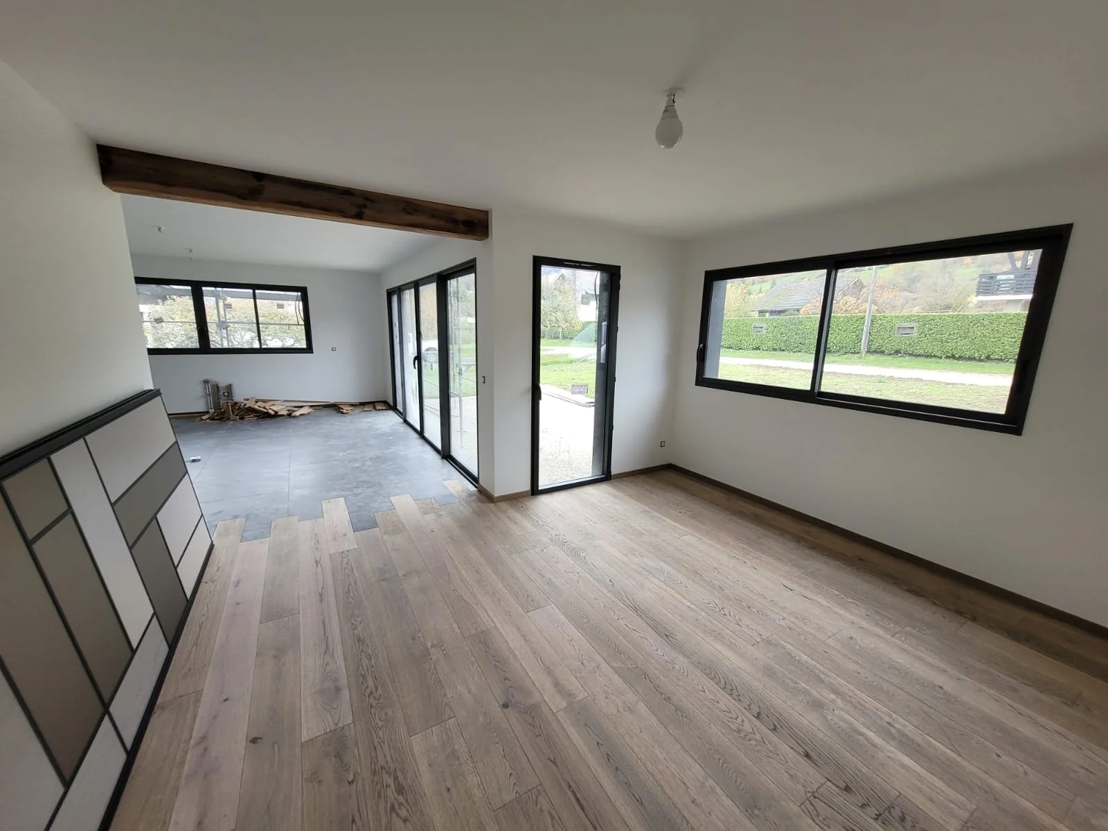 Intérieur d'une maison rénovée avec grandes fenêtres, sol en bois clair et un coin avec des fenêtres coulissantes donnant sur un jardin