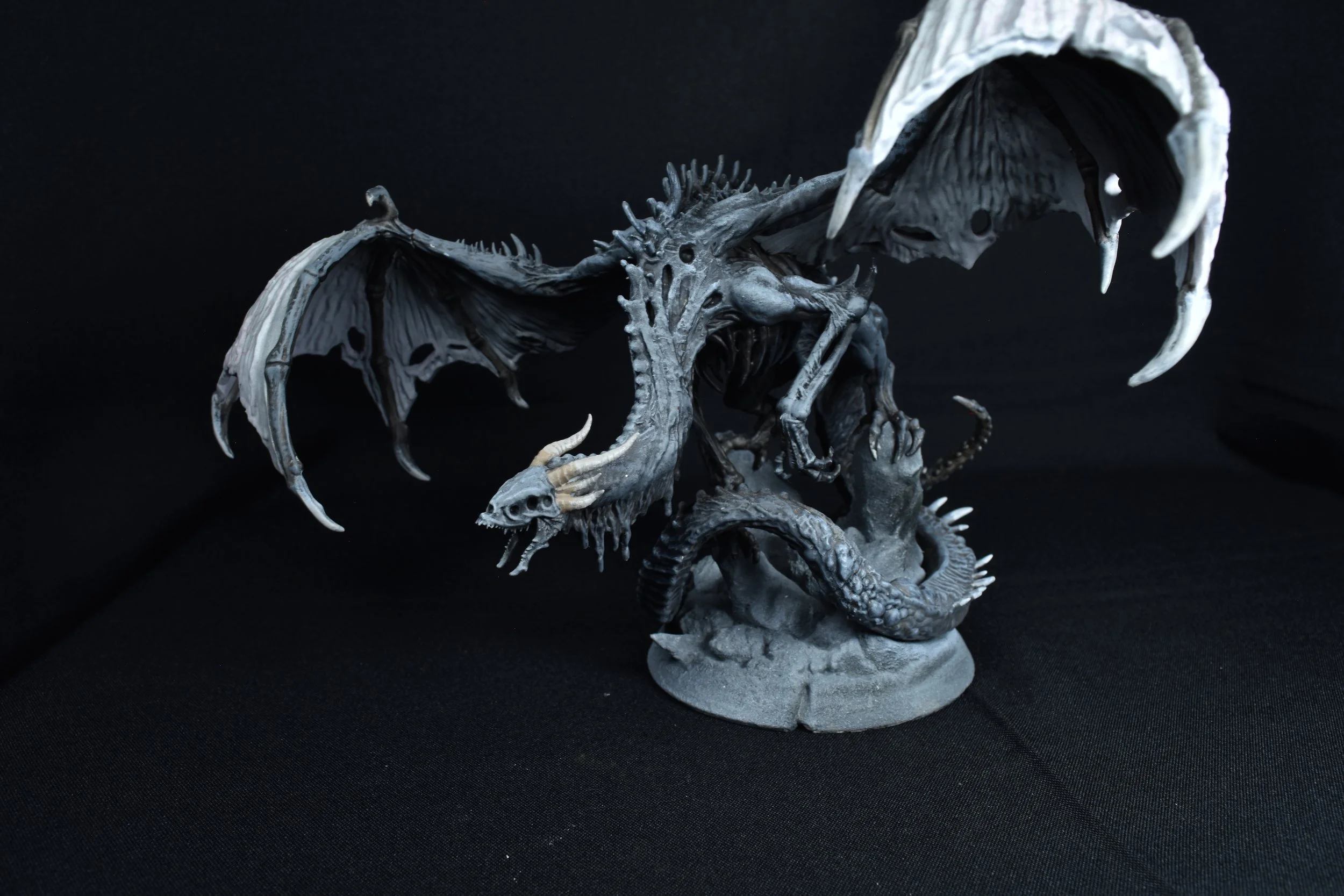 A detailed sculpture of a dragon with large wings and a fierce expression, positioned on a circular base, against a black background.