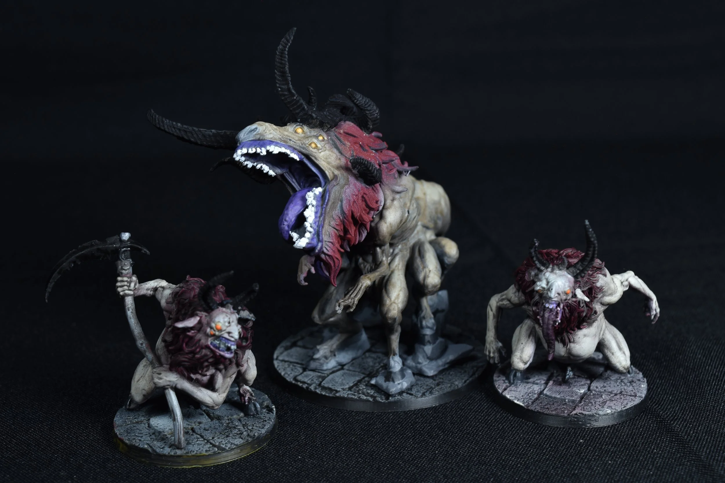 A group of painted miniatures depicting monstrous creatures with animalistic bodies, large horns, sharp teeth, and snarling expressions, set against a dark background.
