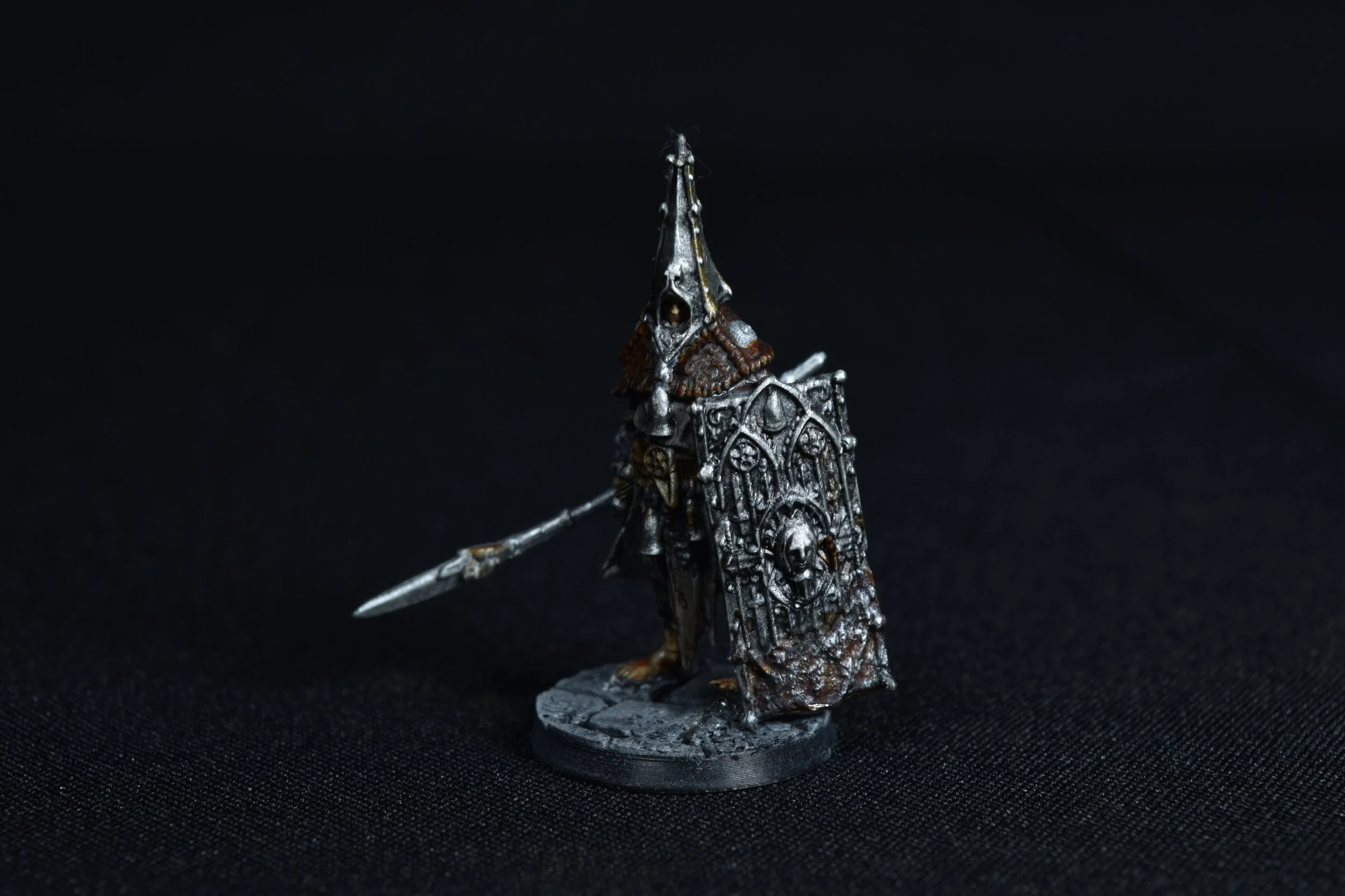 Miniature figurine of a medieval knight in armor, holding a spear, standing on a round base against a black background.