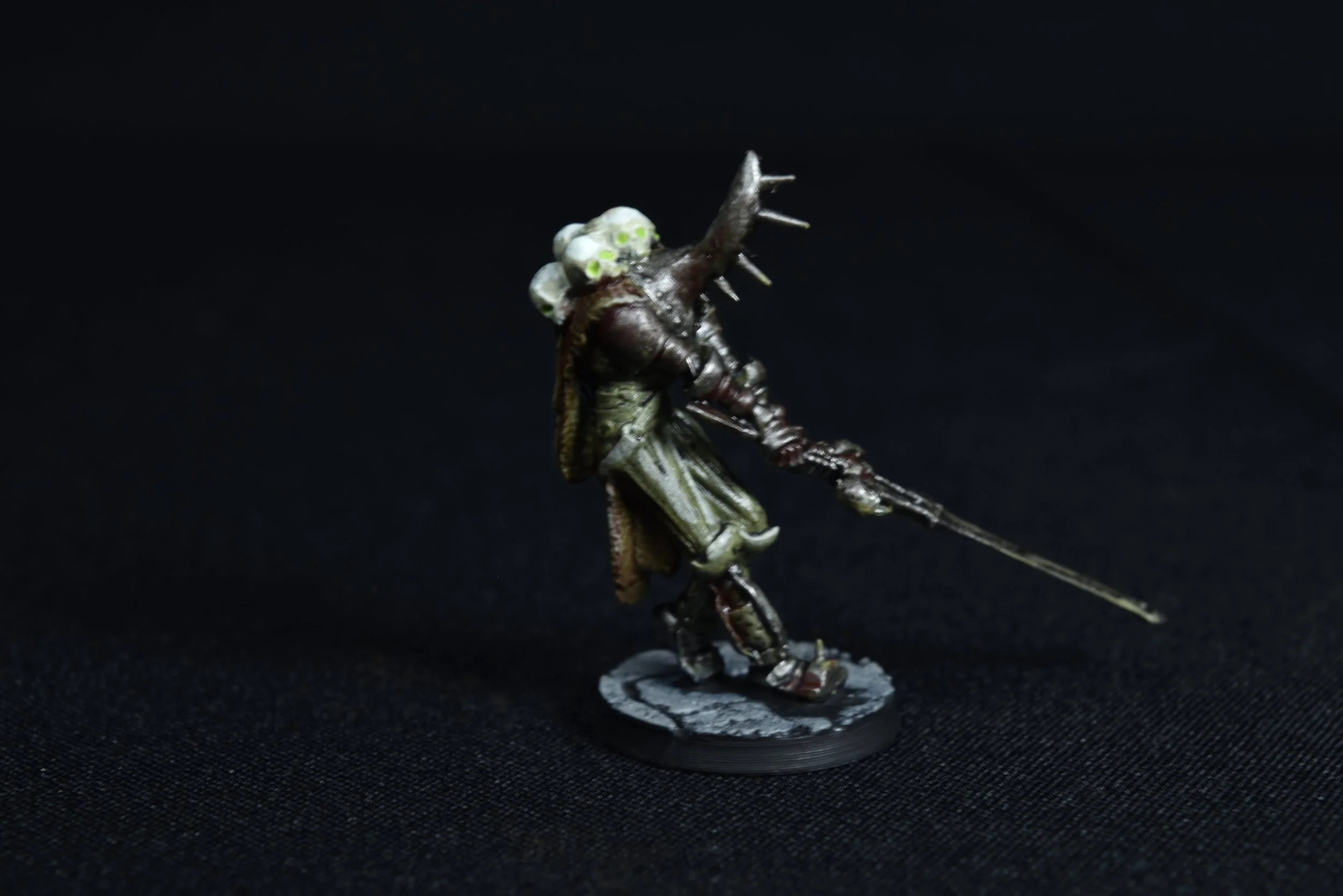 A miniature model of a fantasy soldier with a insect-like appearance, holding a spear, standing on a textured base against a black background.