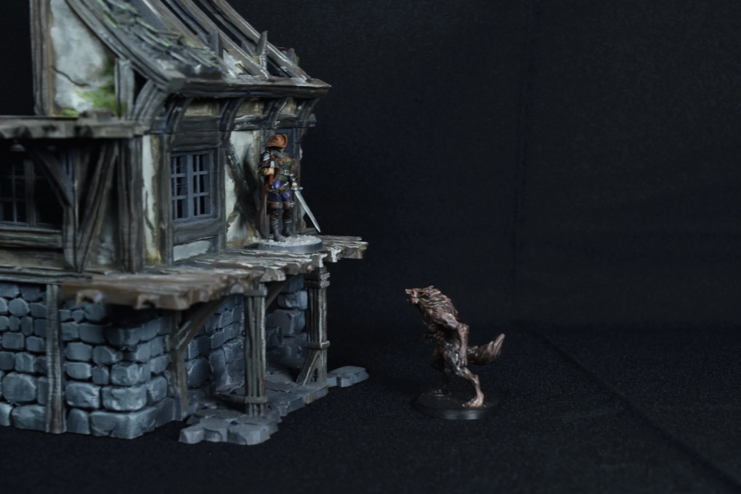 Miniature model scene depicting a medieval-style wooden house on stone foundation, with a knight figure on the balcony, a dragon-like creature below, and a dark background.