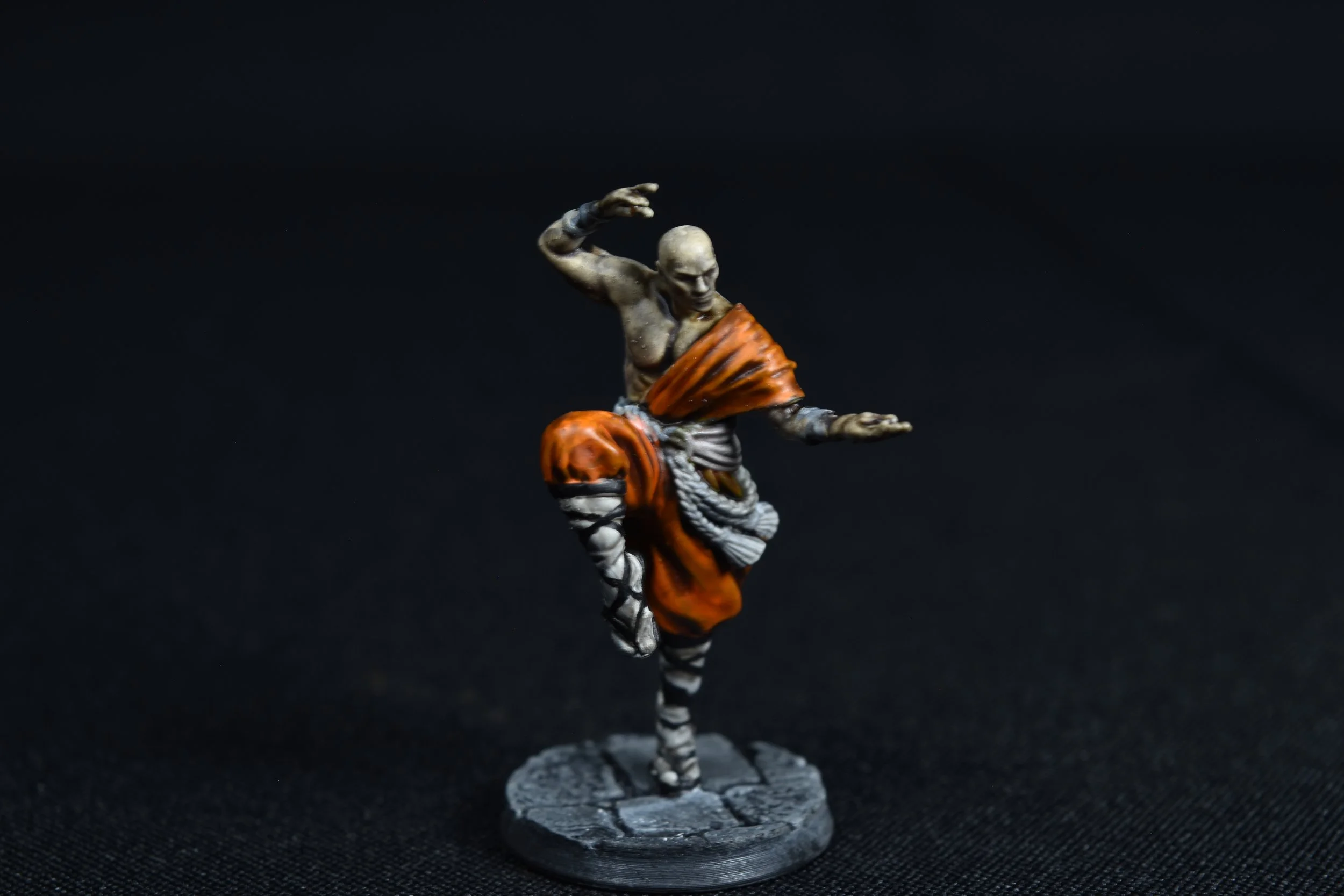 Miniature figurine of a martial artist in an orange outfit performing a high kick against a black background.