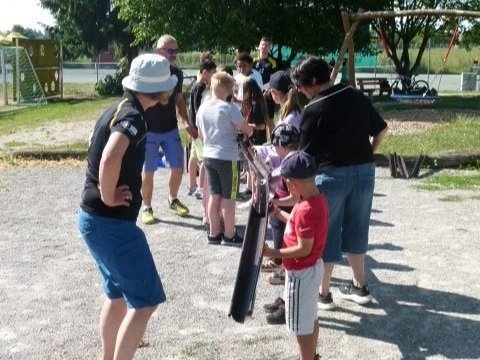 Eine Gruppe von Menschen, hauptsächlich Kinder, versammelt sich im Freien, wahrscheinlich bei einem Spiel oder einer Aktivität im Park.