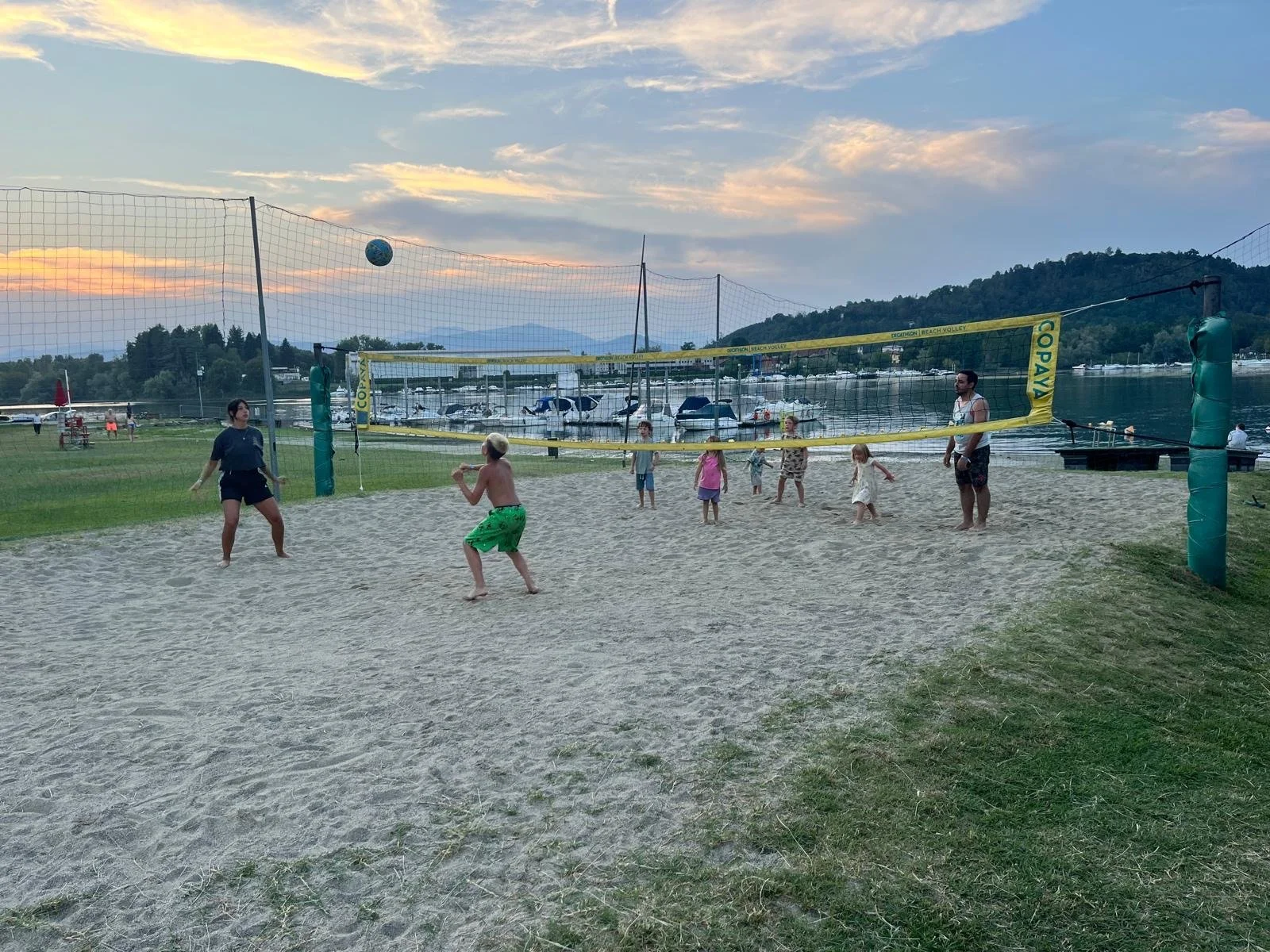 Menschen beim Volleyballspielen auf einem Sandplatz am Wasser bei Sonnenuntergang.