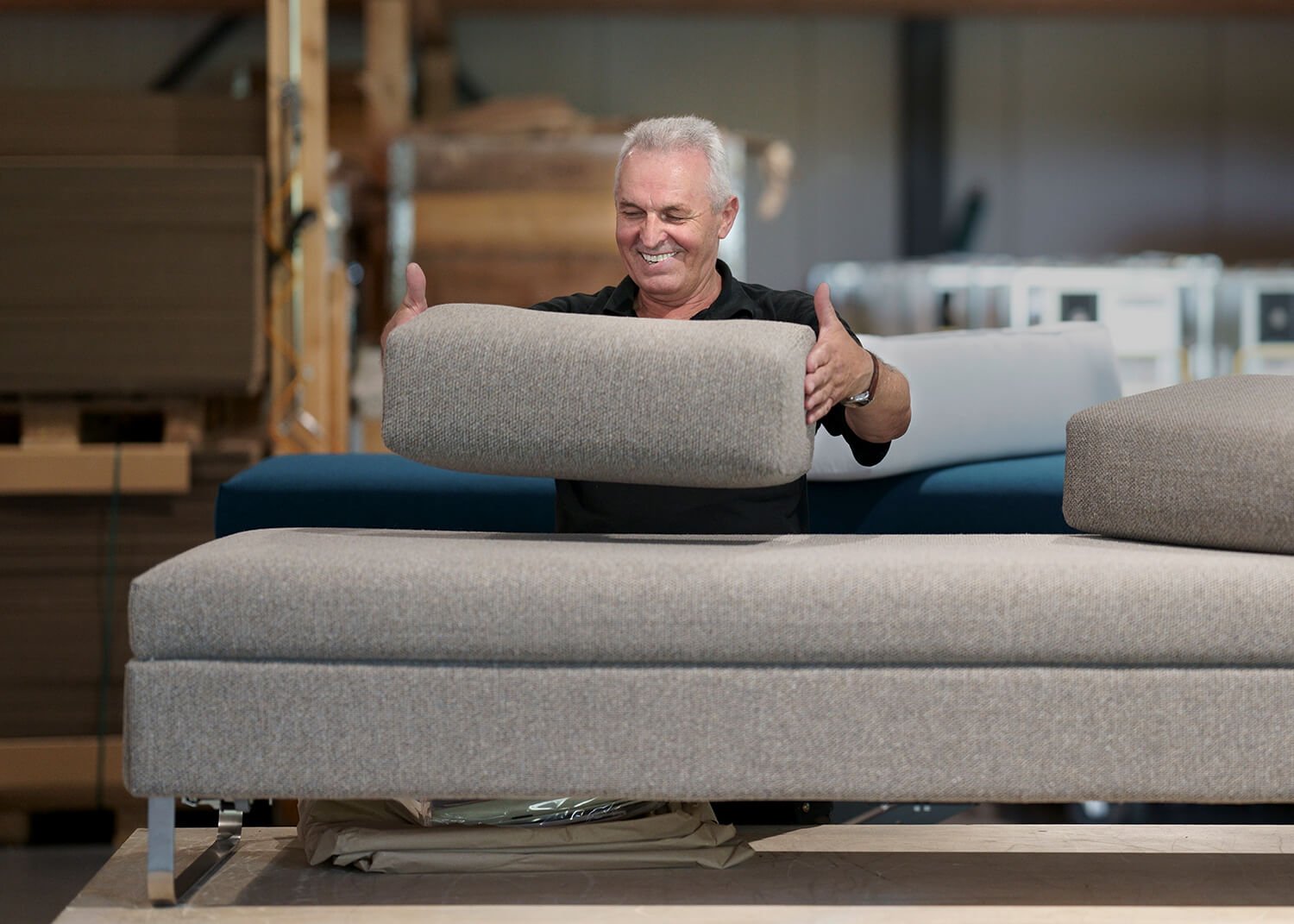 Industriefotografie aus der Produktionshalle der Swiss Plus AG. Ein Mann zeigt freundlich die Stoffe eines Sofas während der Herstellung "made in Switzerland".