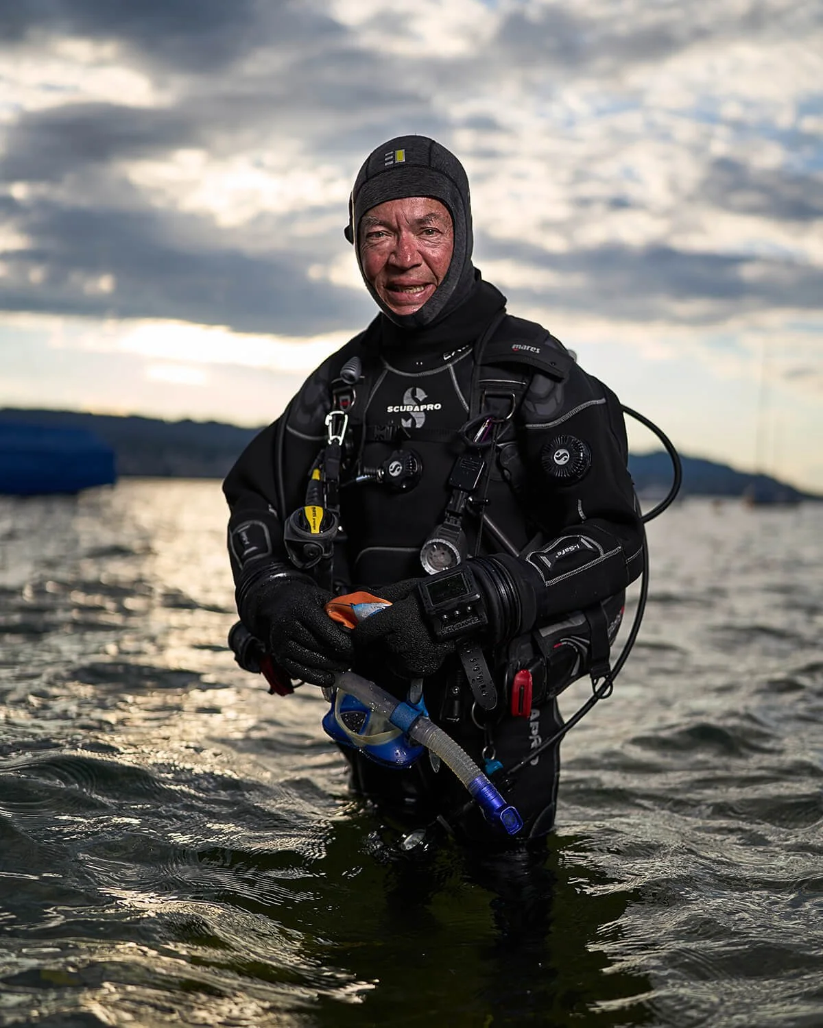 Portraitfotografie eines Taucher im Wasser bei Sonnenuntergang. Er trägt eine Taucherausrüstung und blickt direkt in die Kamera.