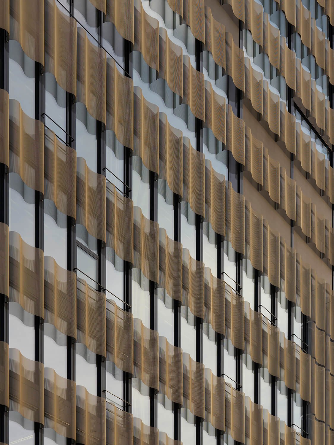 Architekturfotografie einer Fassade eines modernen Gebäudes mit dornenförmigen Blechlamellen in Gold- und Schwarzfarben, die dekorativ an den Fenstern angebracht sind.