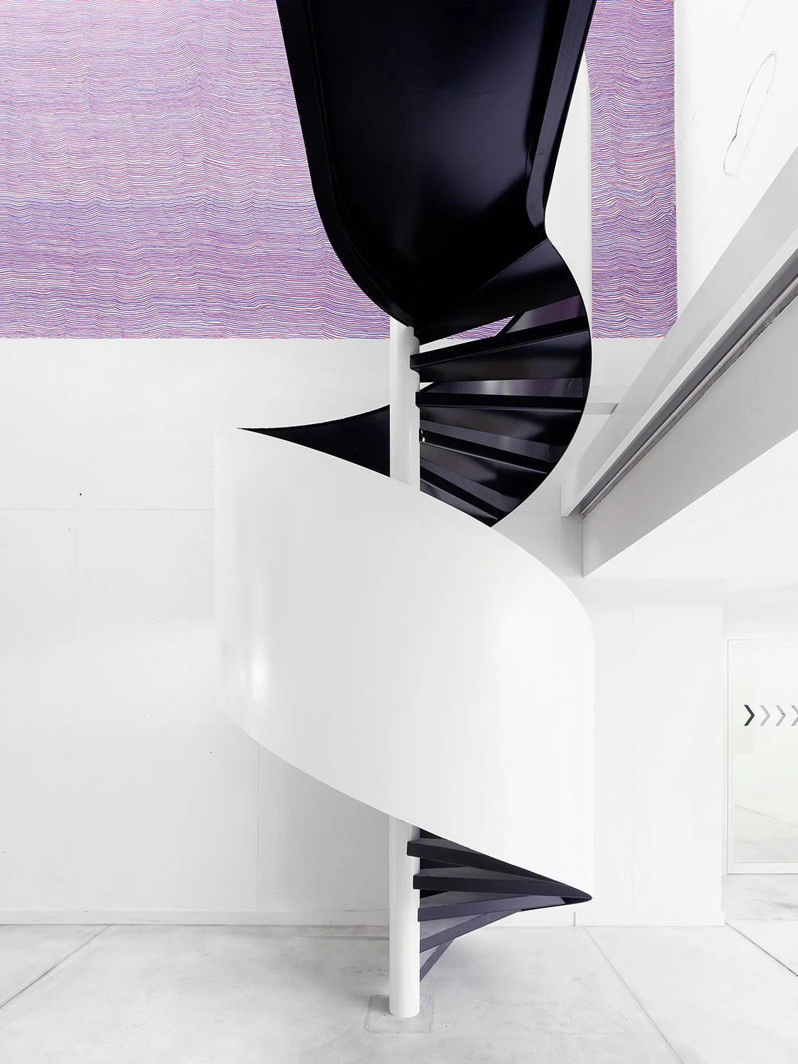 Schwarze Spiraltreppe mit weißen Wänden und Boden, Blick von der Seite.